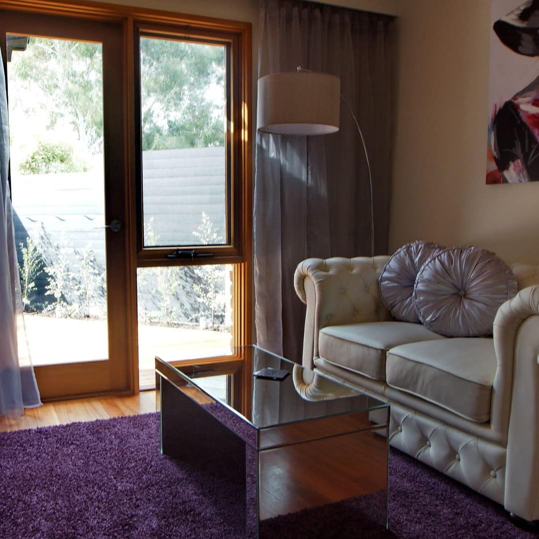 Glam living room with overstuffed white love seat, mirrored coffee table, purple rug and lavender organza curtains