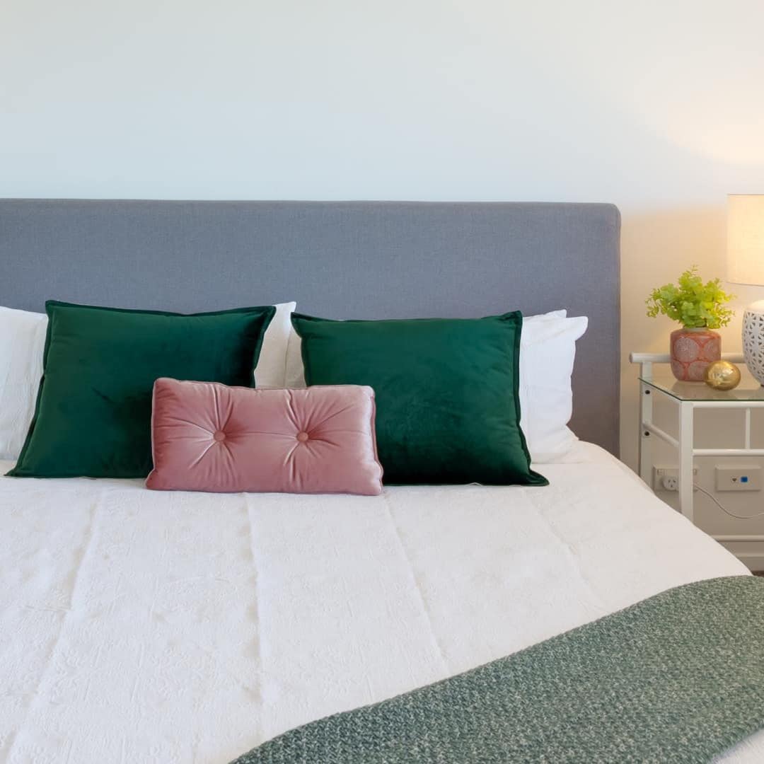 Bedroom with a king size bed, white bedding, green and pink pillows, and matching glass bedside tables.