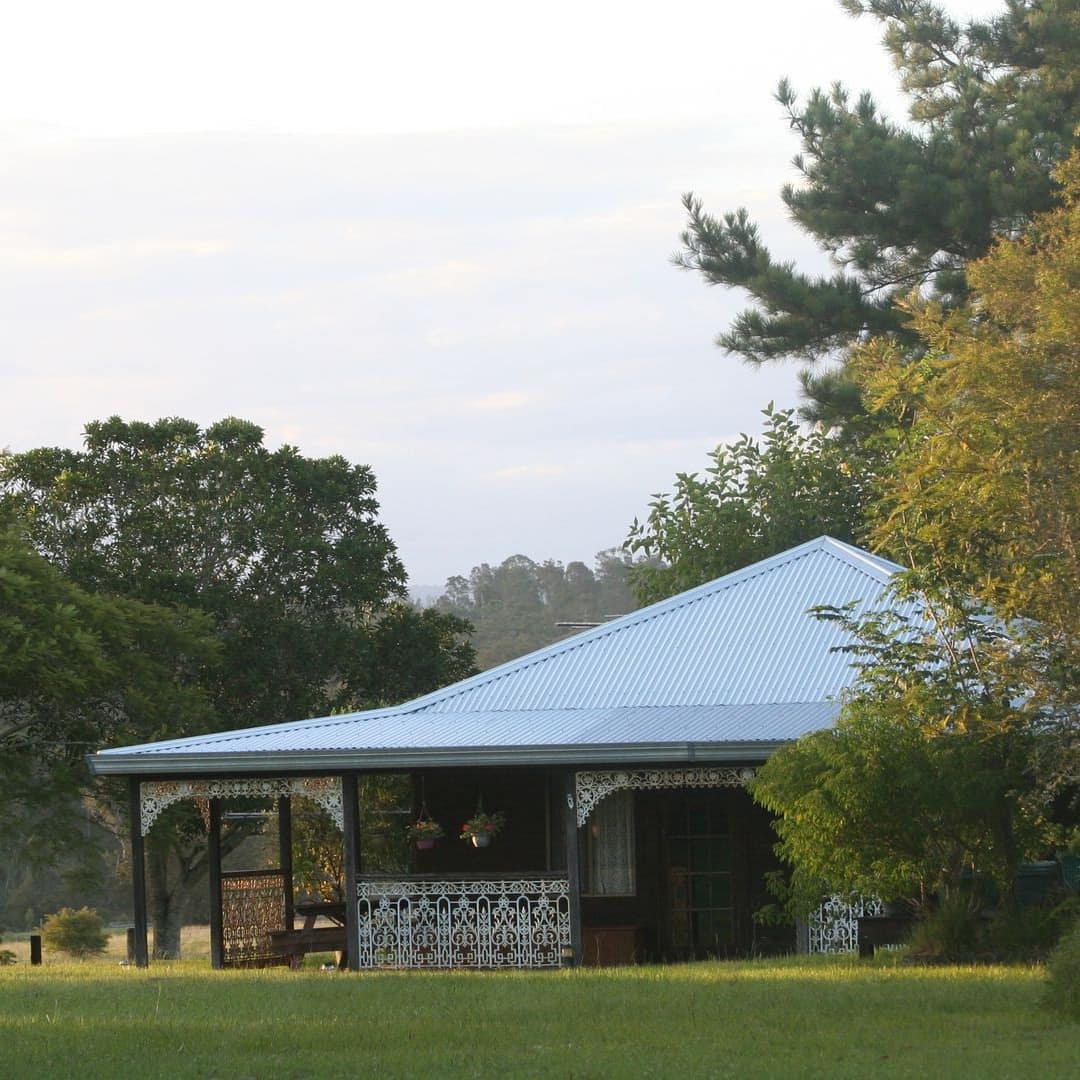 Fairlight Cottage, set in the countryside with a wrap-around porch, and decorative iron porch rails with background trees.