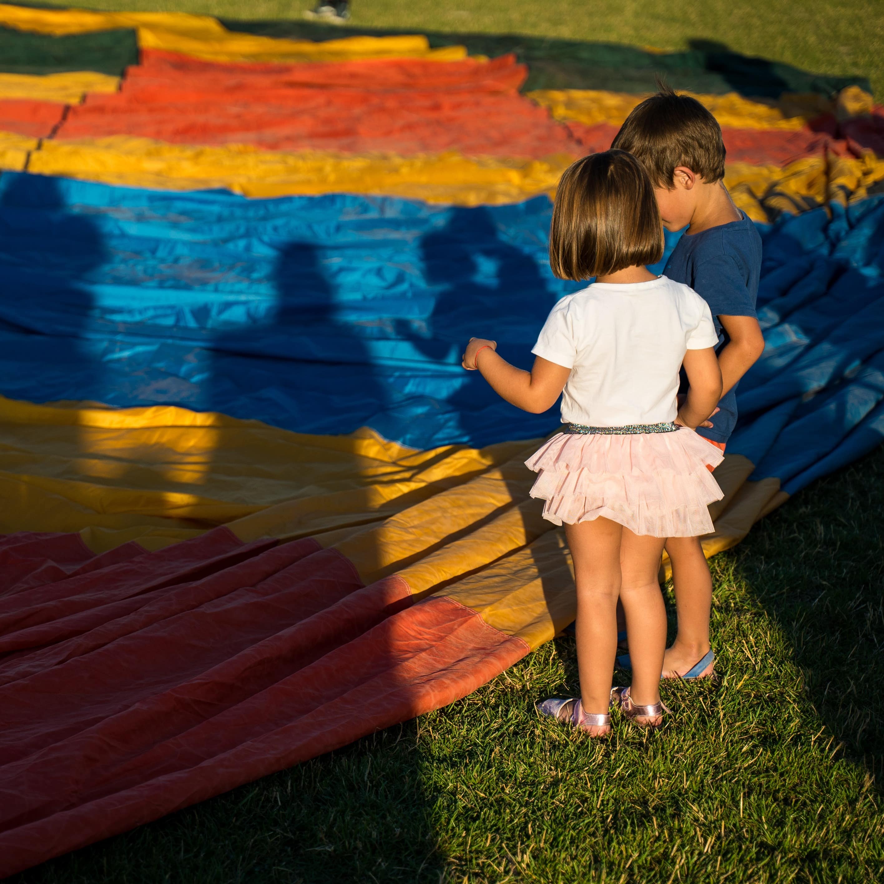 Two young children checking out colorful hot air balloon textile on the ground before they go for ride