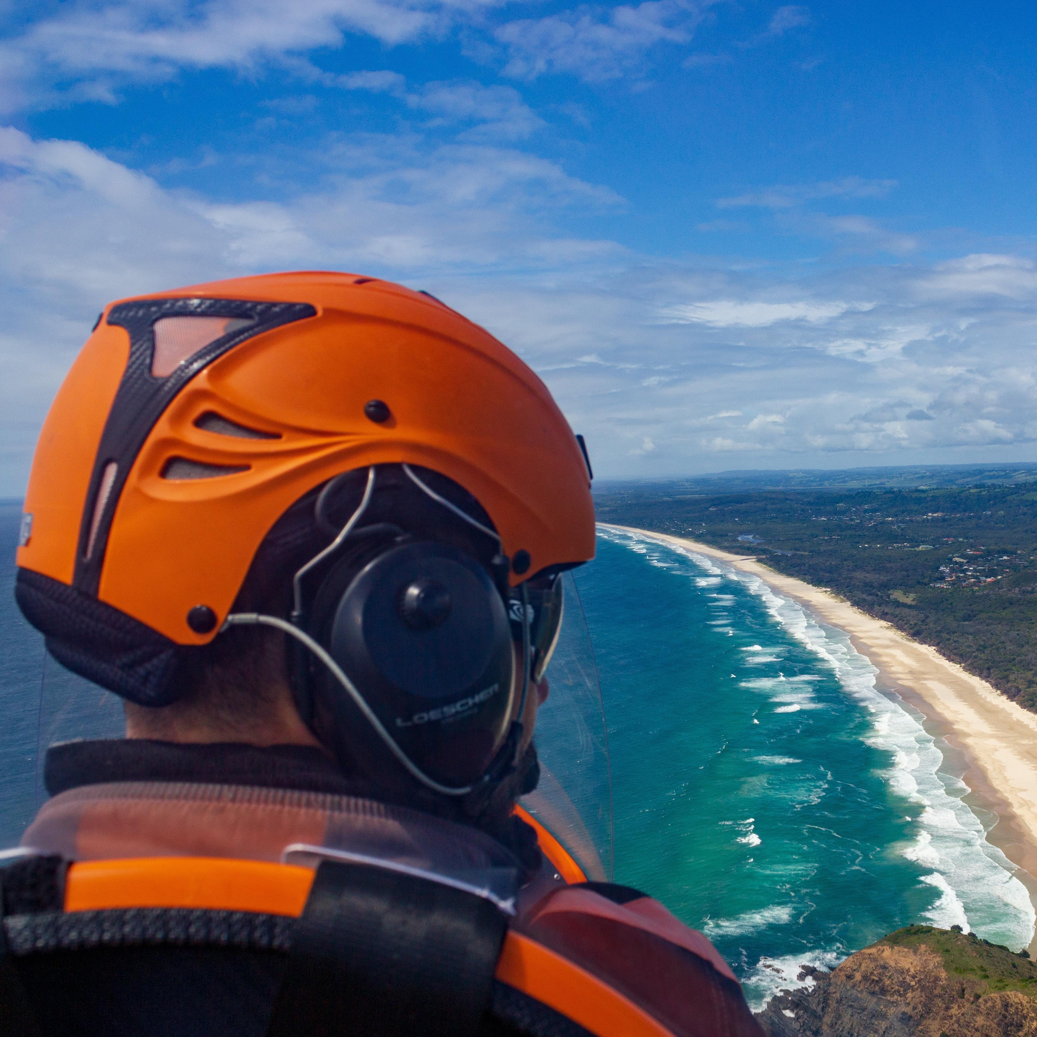 The head of a pilot with orange helmet flying a gyrocopter over Byron Bay, Queensland, Australia