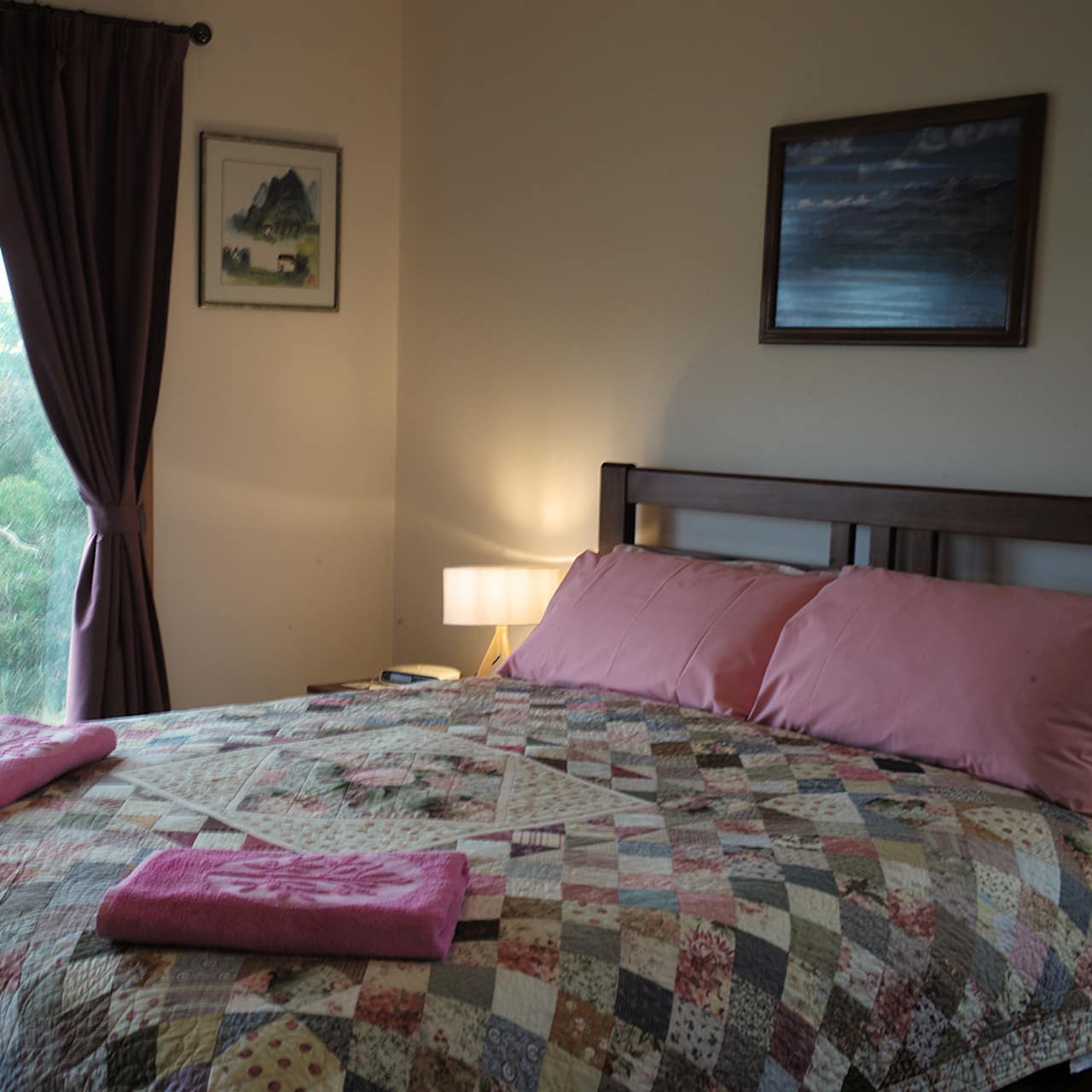 Bedroom with beige walls, king size bed, colorful quilt, wide window with views of rural landscape.