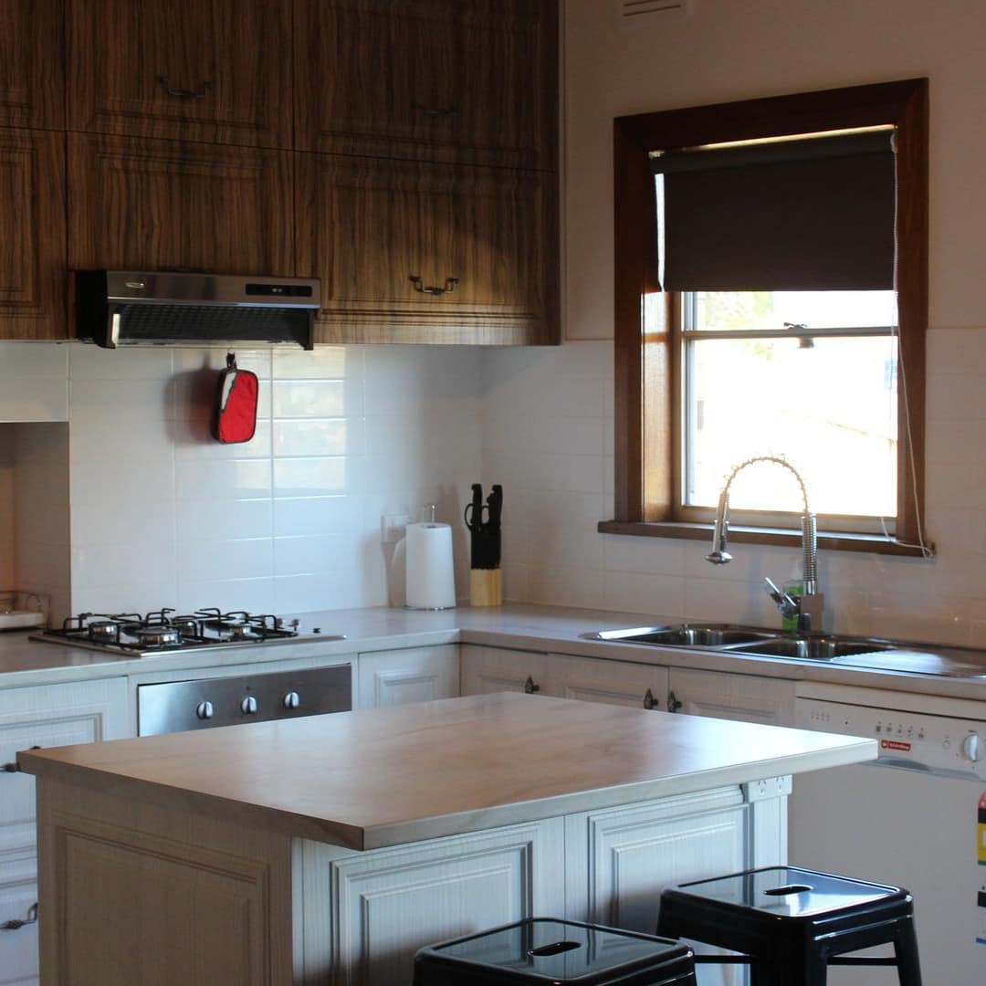 Open kitchen with white cabinets and white tile backsplash and a kitchen island with black bar stools.