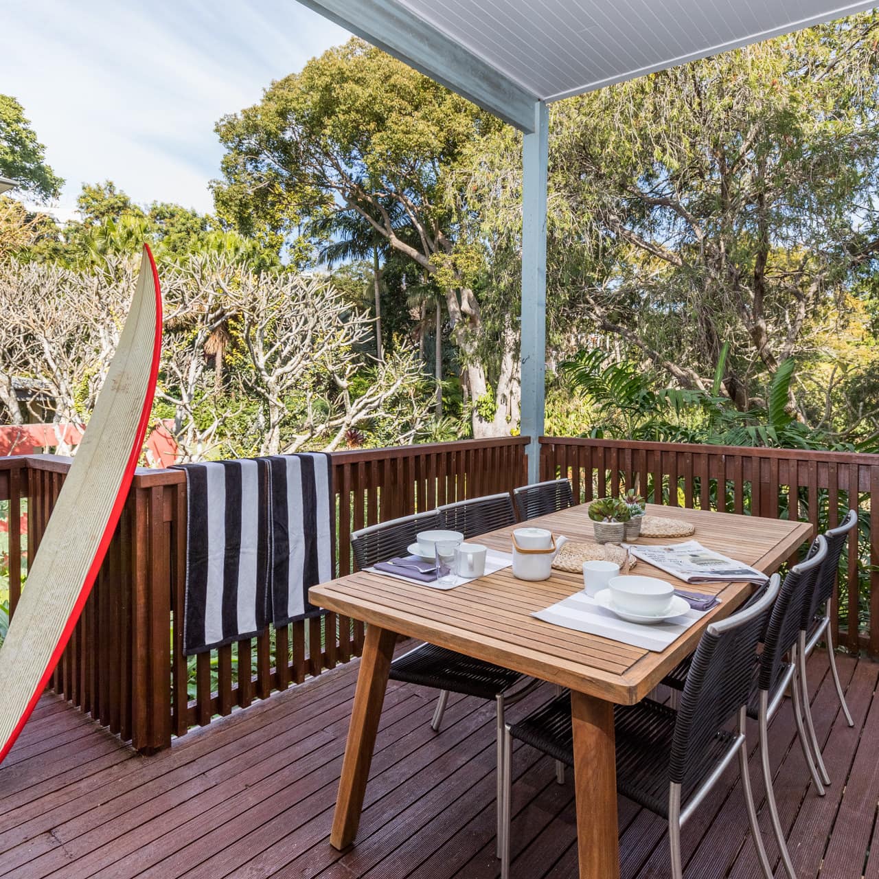 A wooden deck with a dining table and black chairs, surrounded by thick forest.
