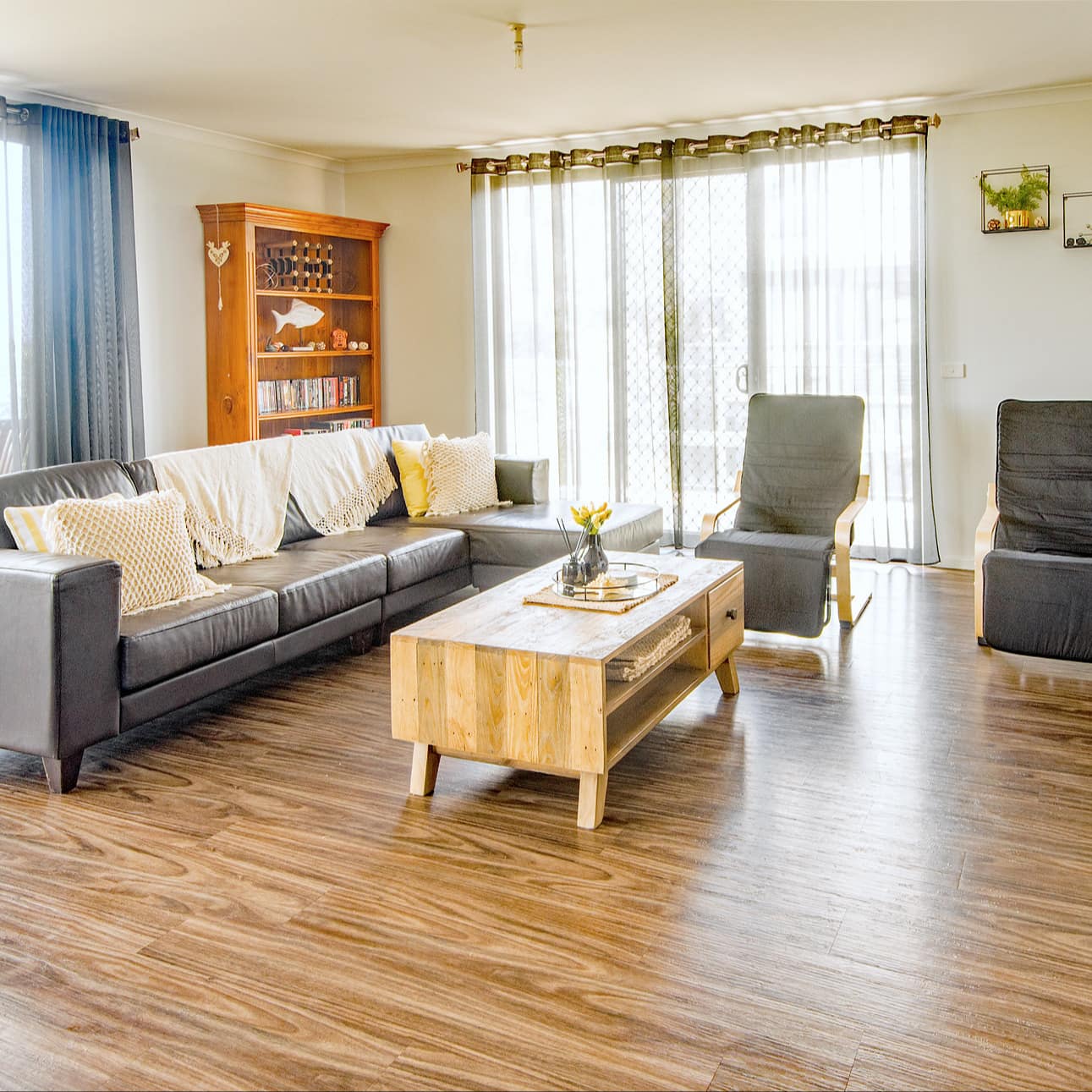 Open living room with hardwood floors, black leather sofa and black chairs, wooden coffee table, tall windows.