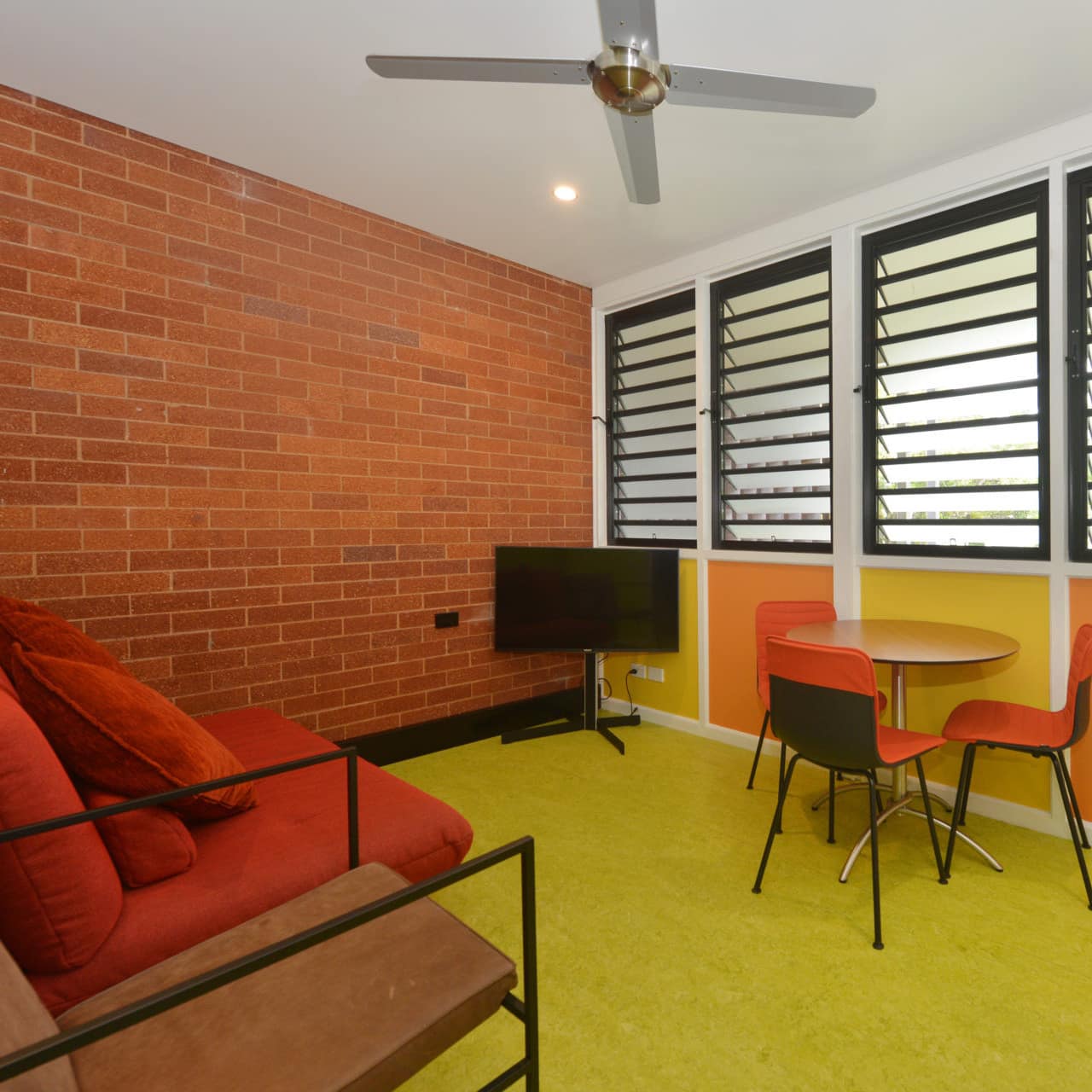 Retro living room with green carpet, brick walls, red sofa, small dining set, and a flatscreen TV.