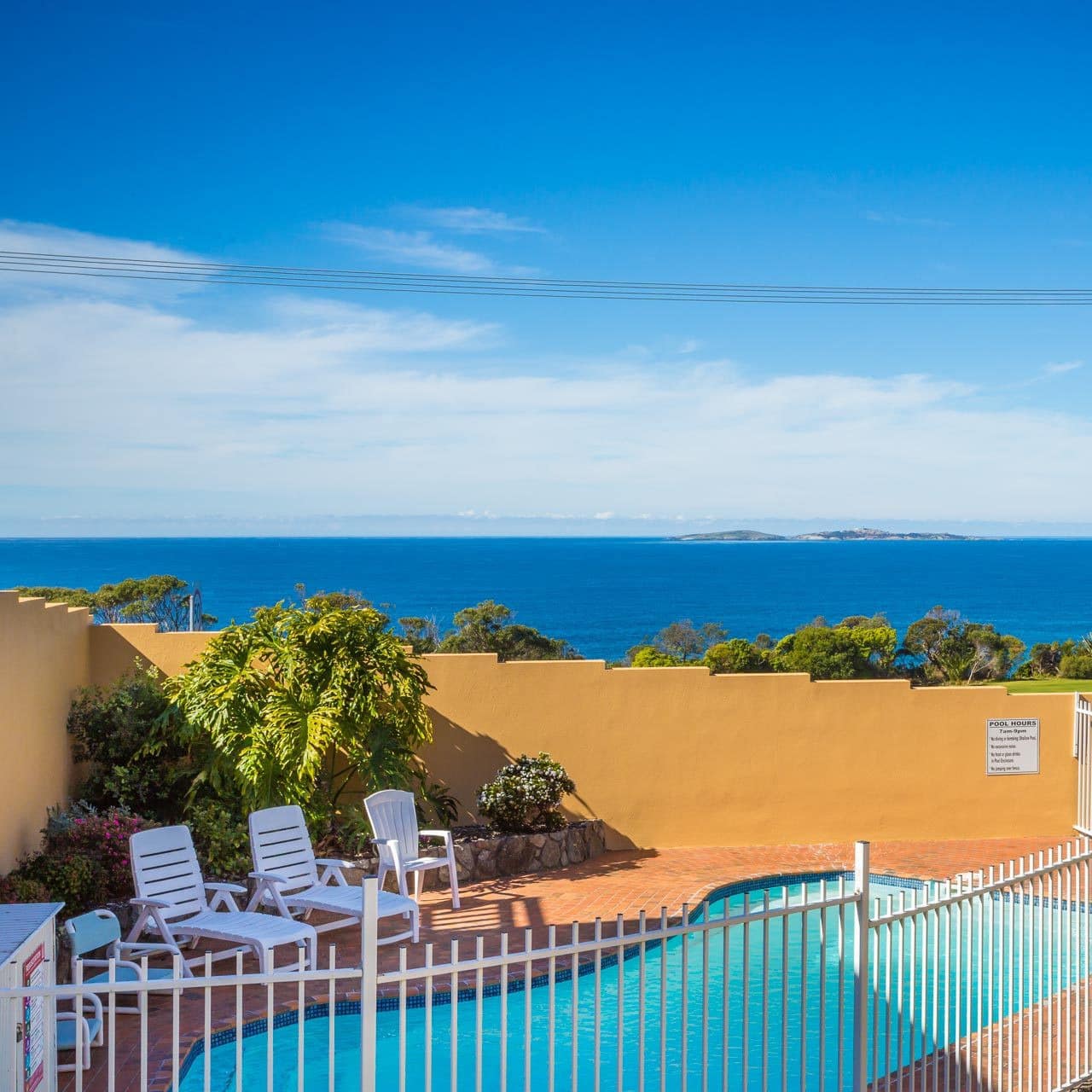 A brick patio space with inground pool and white lounge chairs overlooking the golf course and ocean.