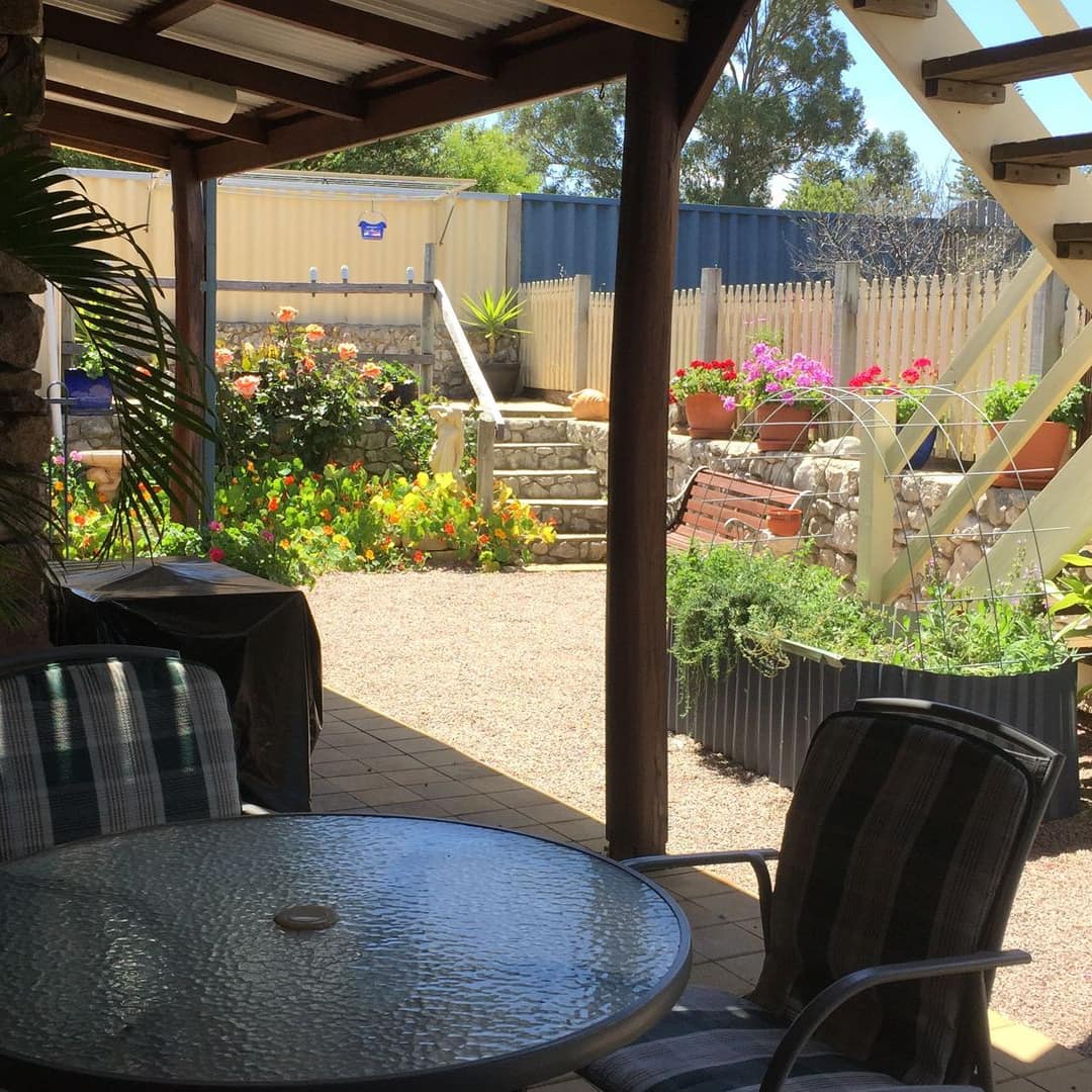 A patio garden with a glass-top table, chairs, a grill and colourful potted plants.
