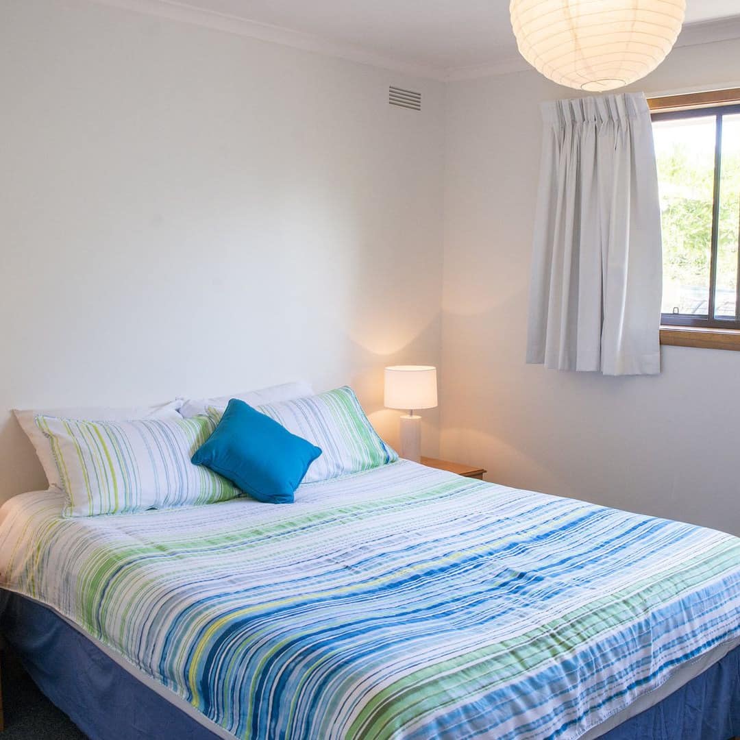 Sunny bedroom with a king-size bed, blue and green striped bedding, wooden bedside tables, paper lantern overhead light.