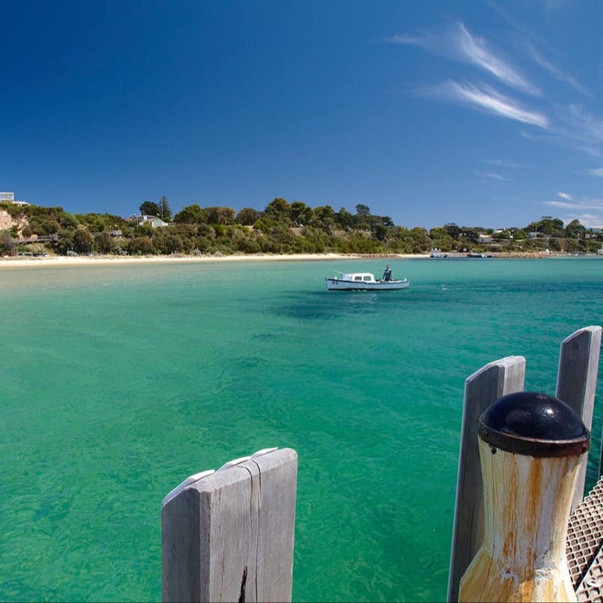 View of the beach and a boat in the ocean from a pier.