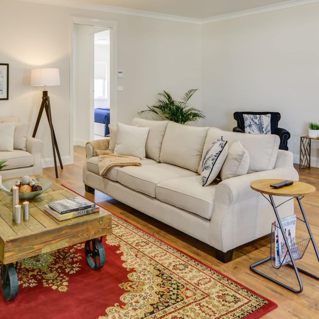 Open living room with beige canvas sofas, navy blue chairs, antique wood coffee table, and red and gold persian rug.