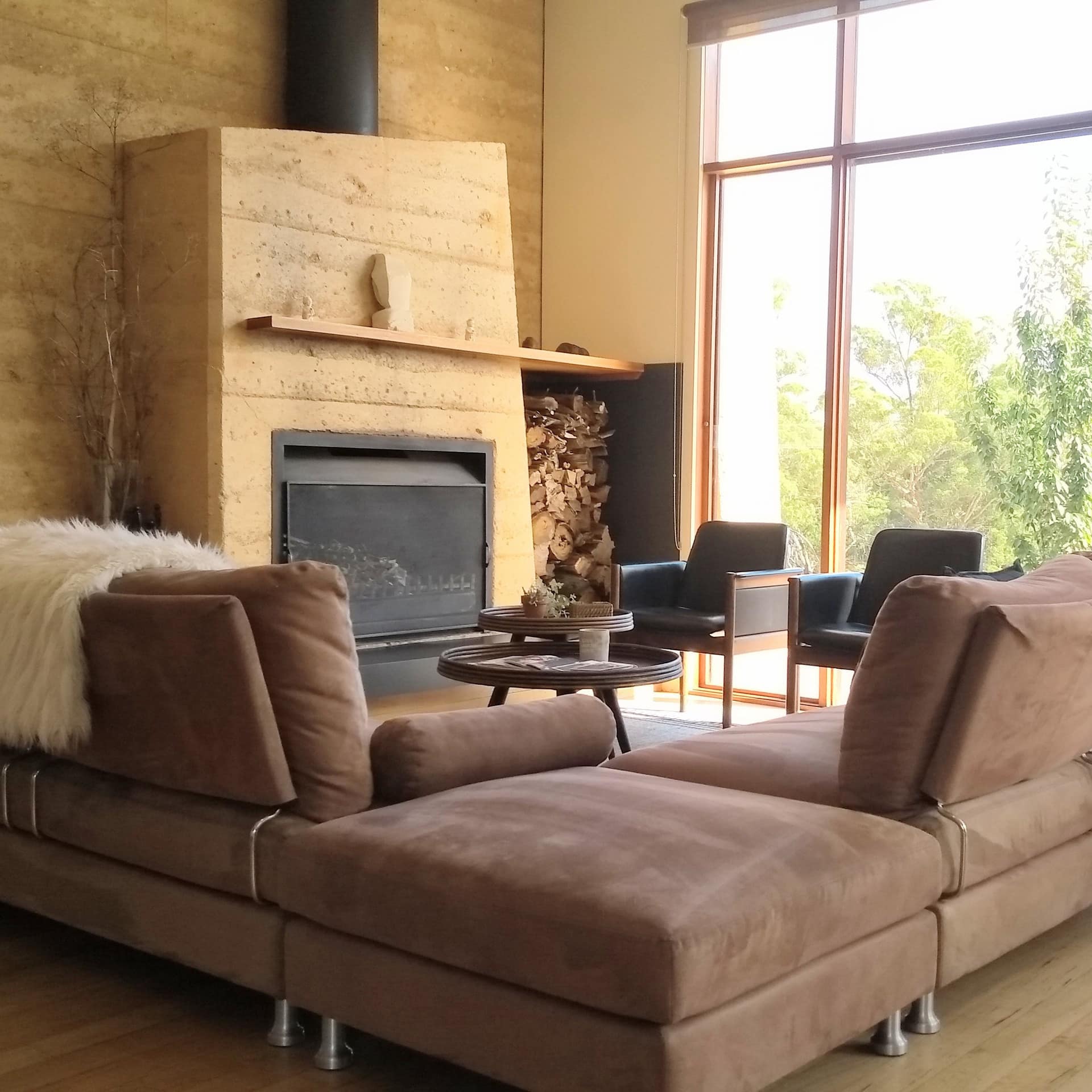 Open living room with hardwood floors, wood-panelled walls, brown suede sectional, fireplace, and tall windows.