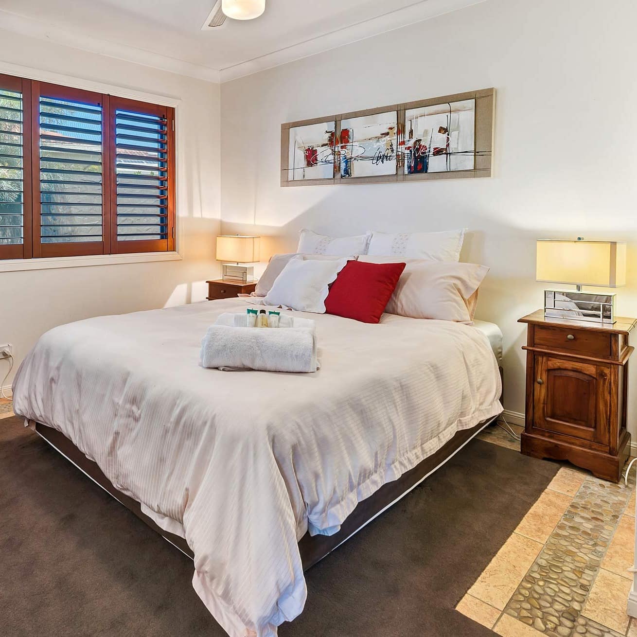Bedroom with stone tile floors, a king size bed, white bedding, and vintage furniture.