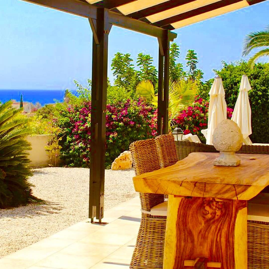 Veranda of 4-bedroom luxury villa with outdoor wooden dining table and wicker chairs surrounded by blooming garden