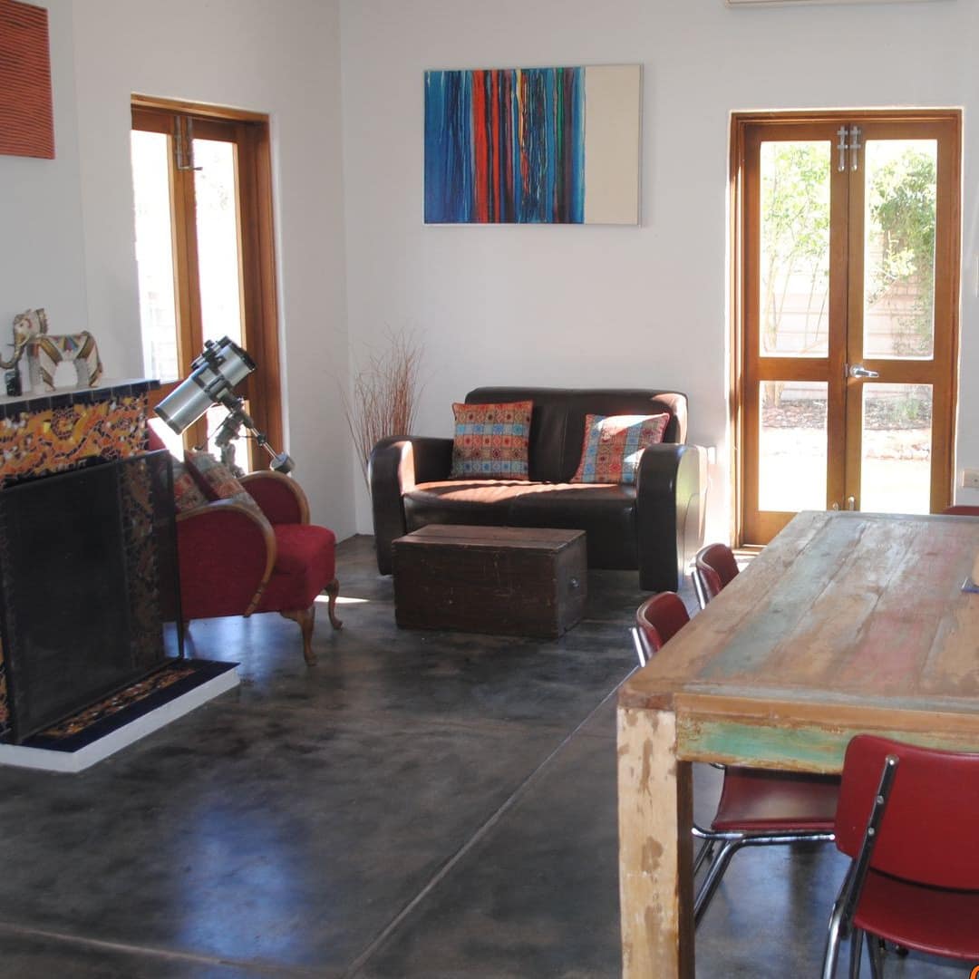 Open dining and living room with reclaimed wood dining table and red chairs, grey stone tile floors, and fireplace.