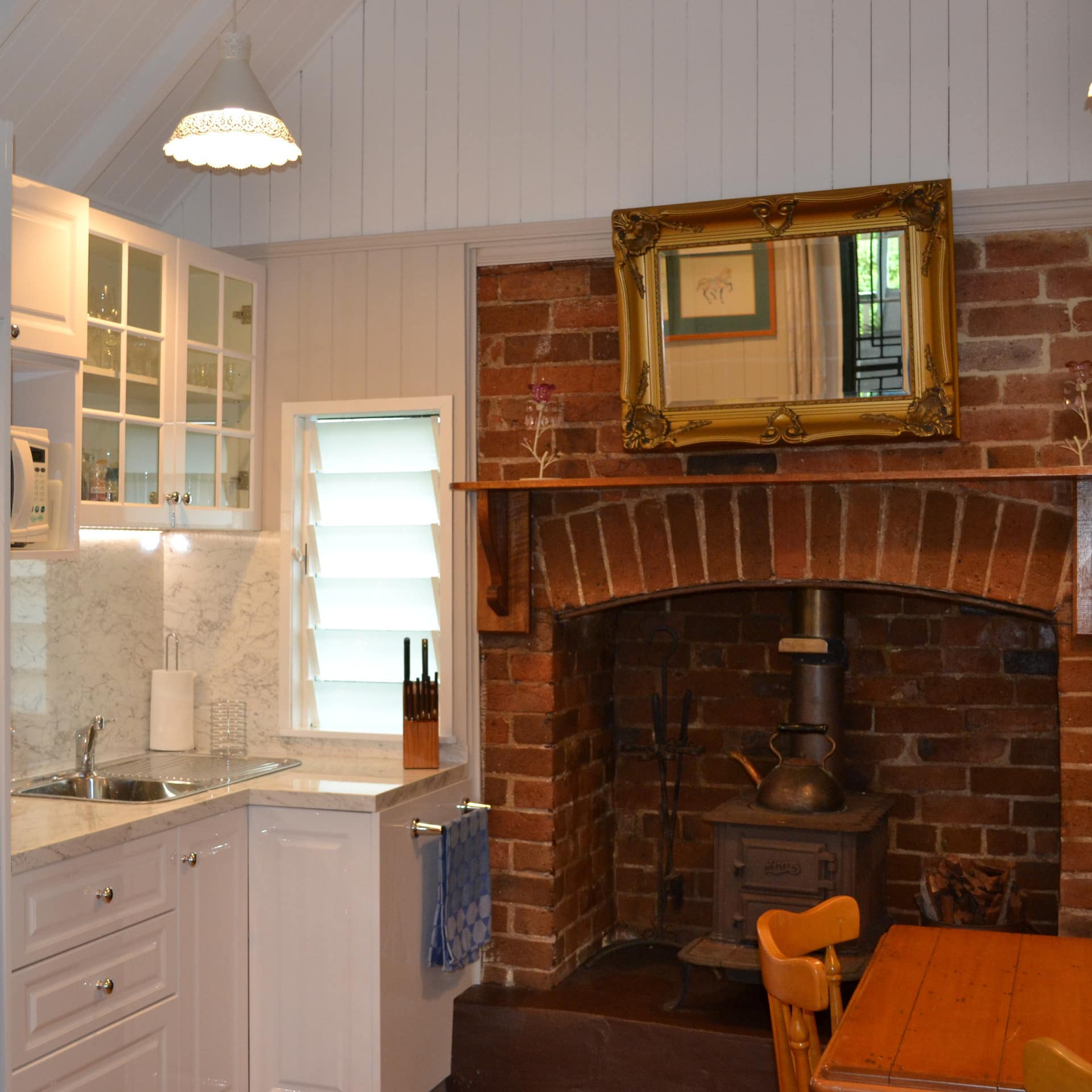 Charming kitchen with brick fireplace, wood dining set, white cabinets, and marble countertops.