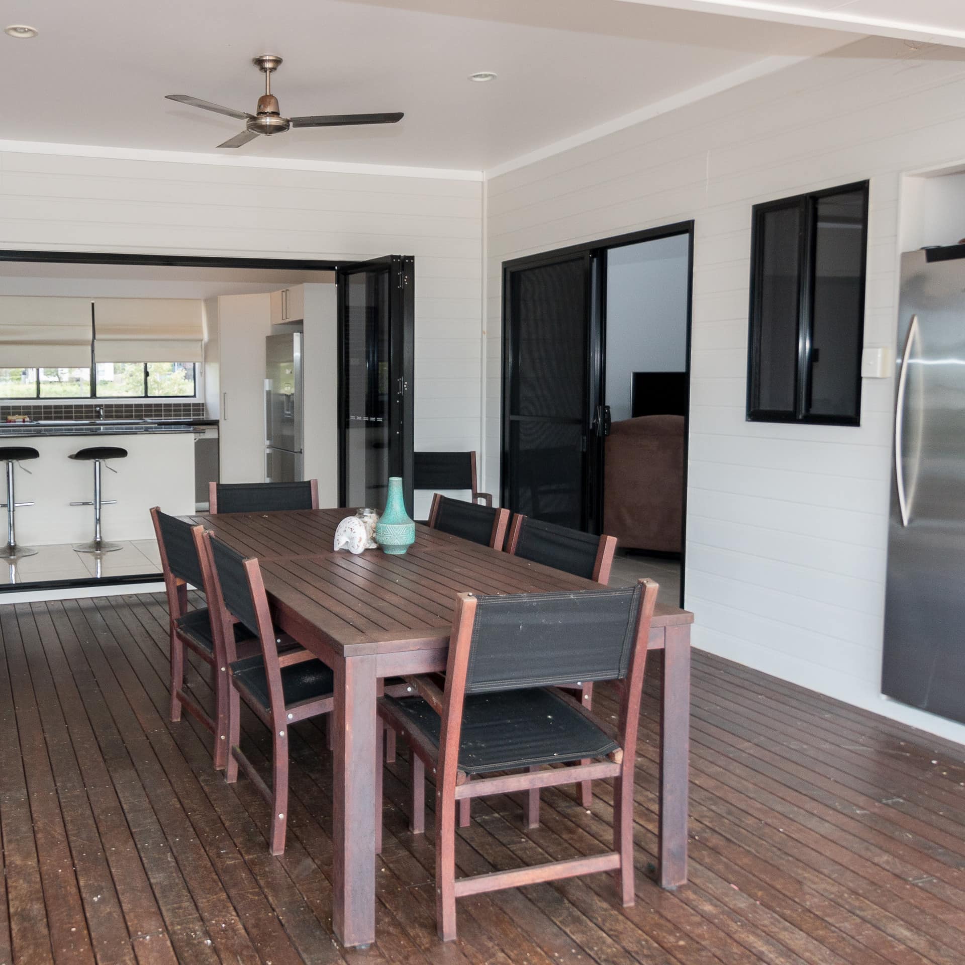 Outdoor dining room on covered deck with hardwood floors, wood dining set, and glass folding doors open into the kitchen.