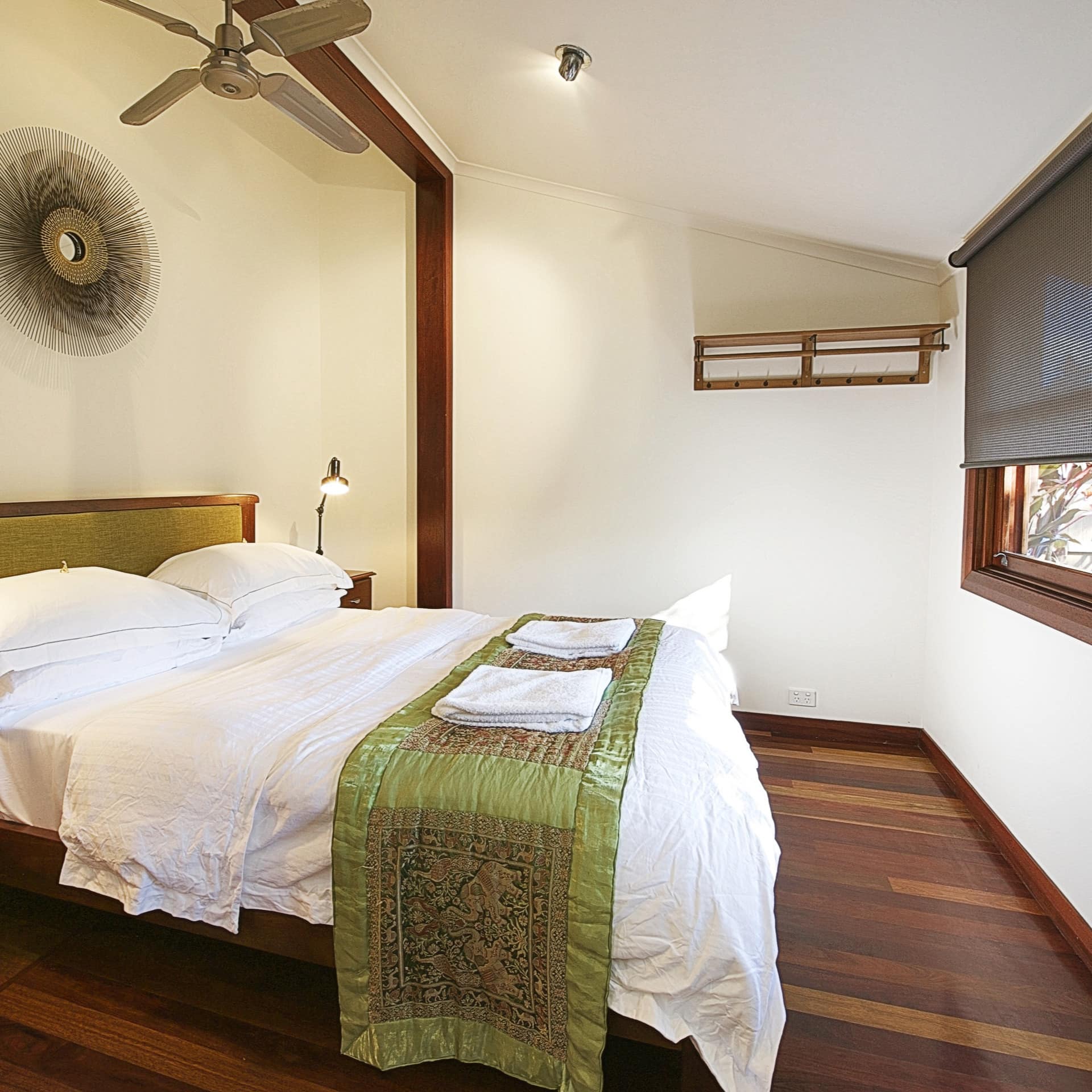 Bedroom with hardwood floors, white walls, a king size bed, white and green bedding, wide windows, roller blinds.