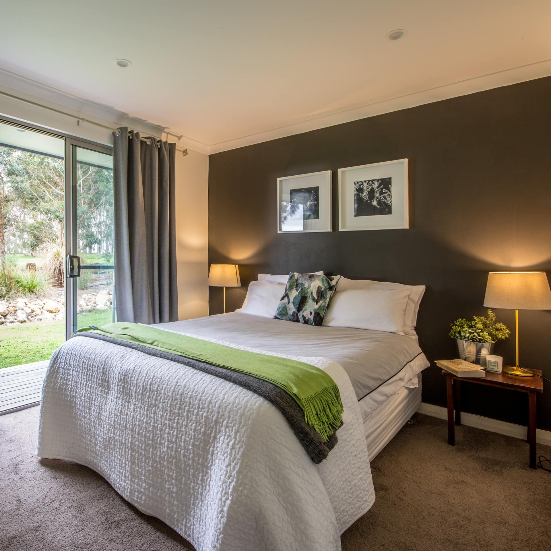 Bedroom with grey carpet and grey accent wall, a king size bed with grey and green bedding, sliding glass doors to backyard.