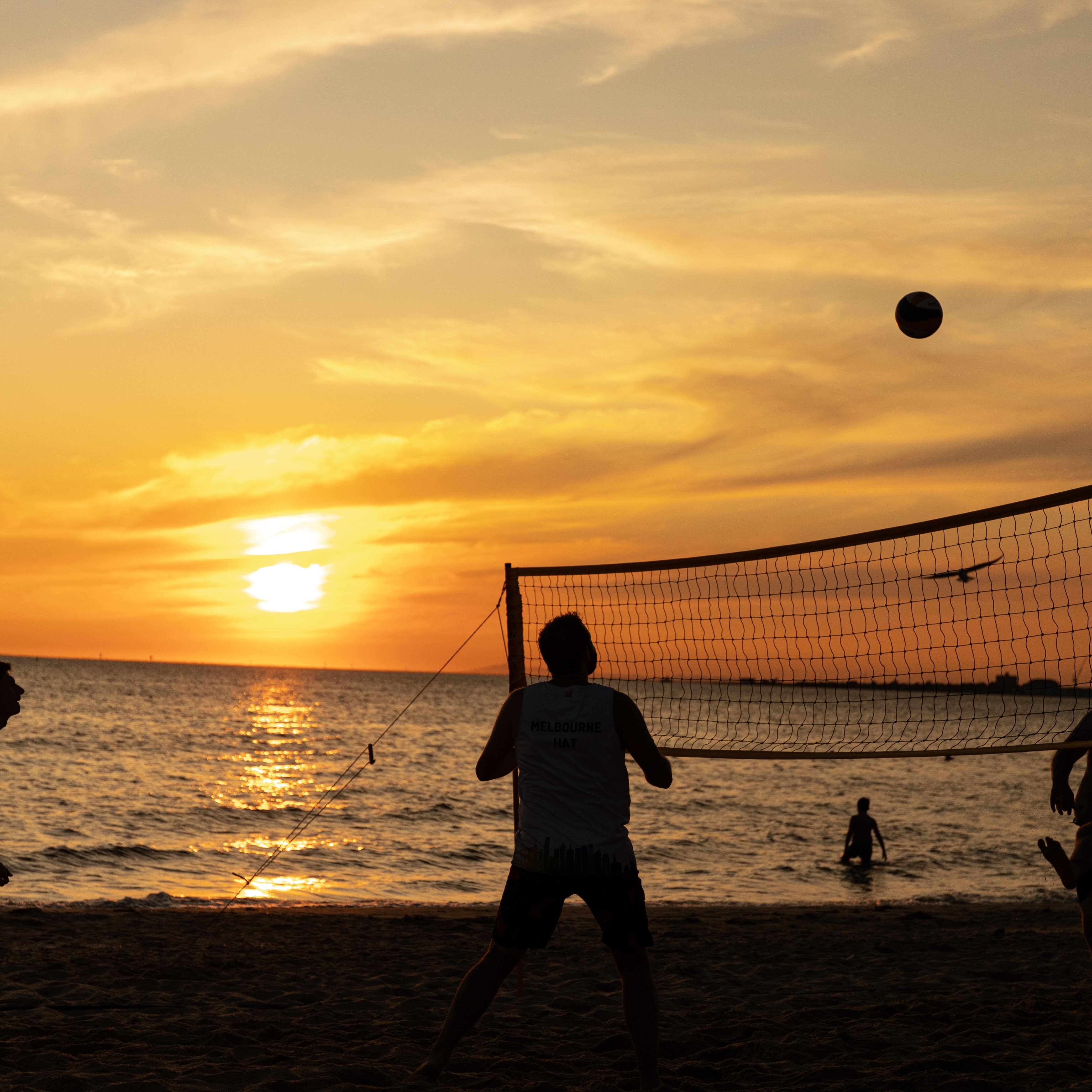 Silhouettes of three people playing beach volleyball against the sunset at the beach