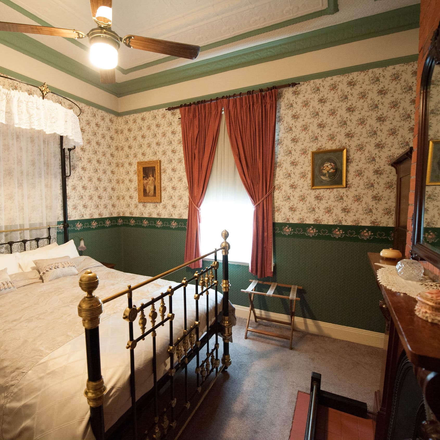 Antique bedroom with hardwood floors, floral wallpaper, metal canopy bed, white bedding, lace canopy and a fireplace.