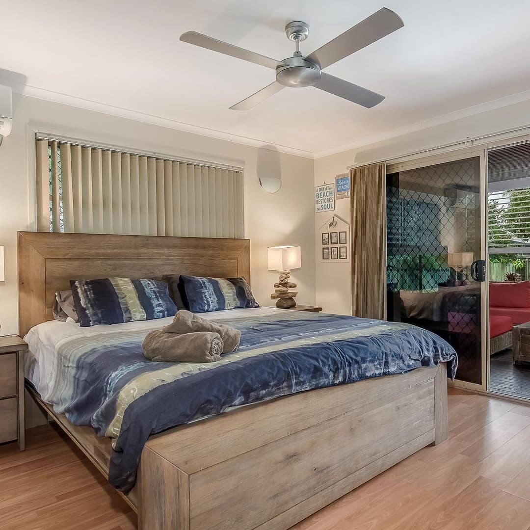 Bedroom with hardwood floors, a wood-framed king size bed, blue and white bedding, sliding glass doors to patio.