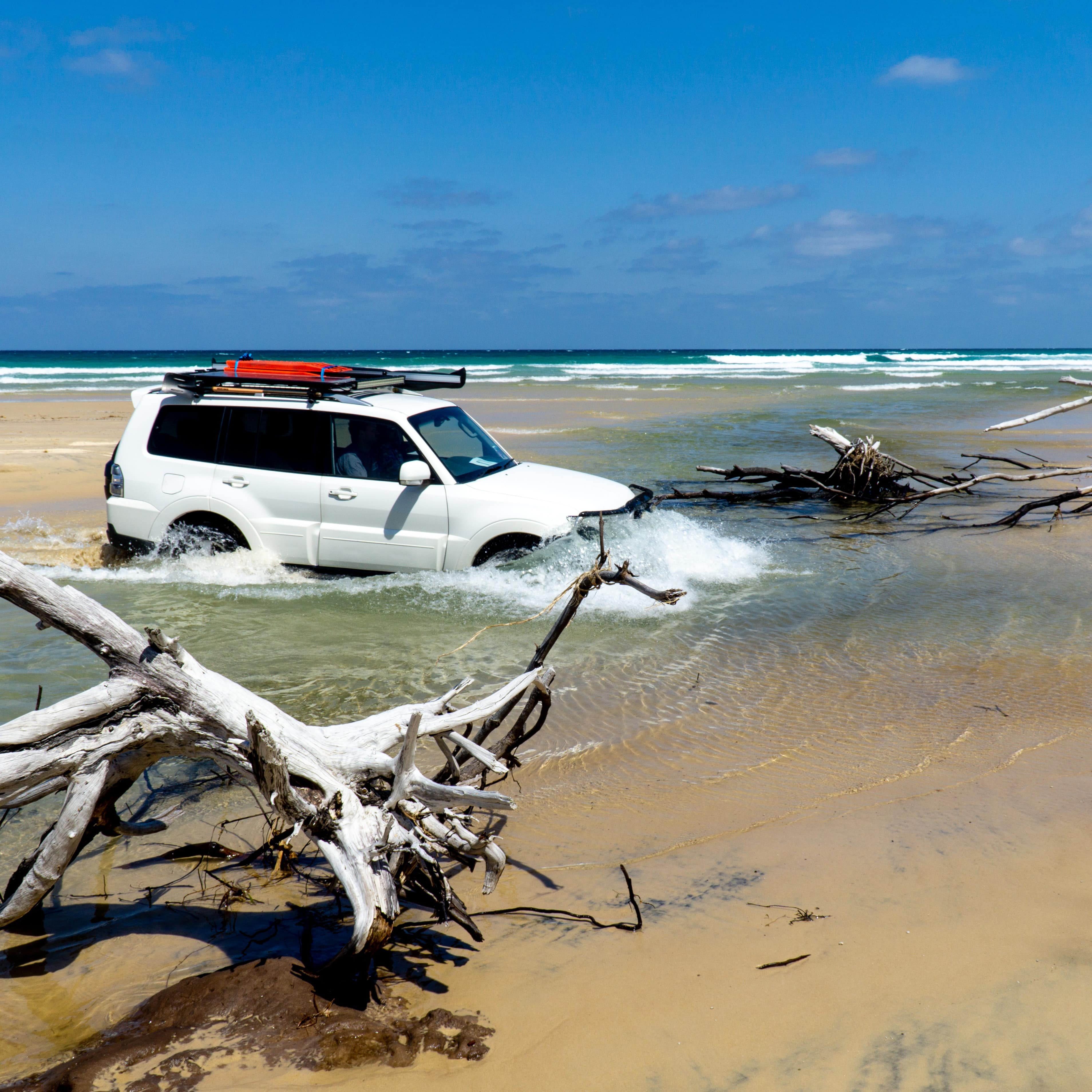 4 wheel drive vehicle splashing through ocean puddles on the beach between washed up driftwood