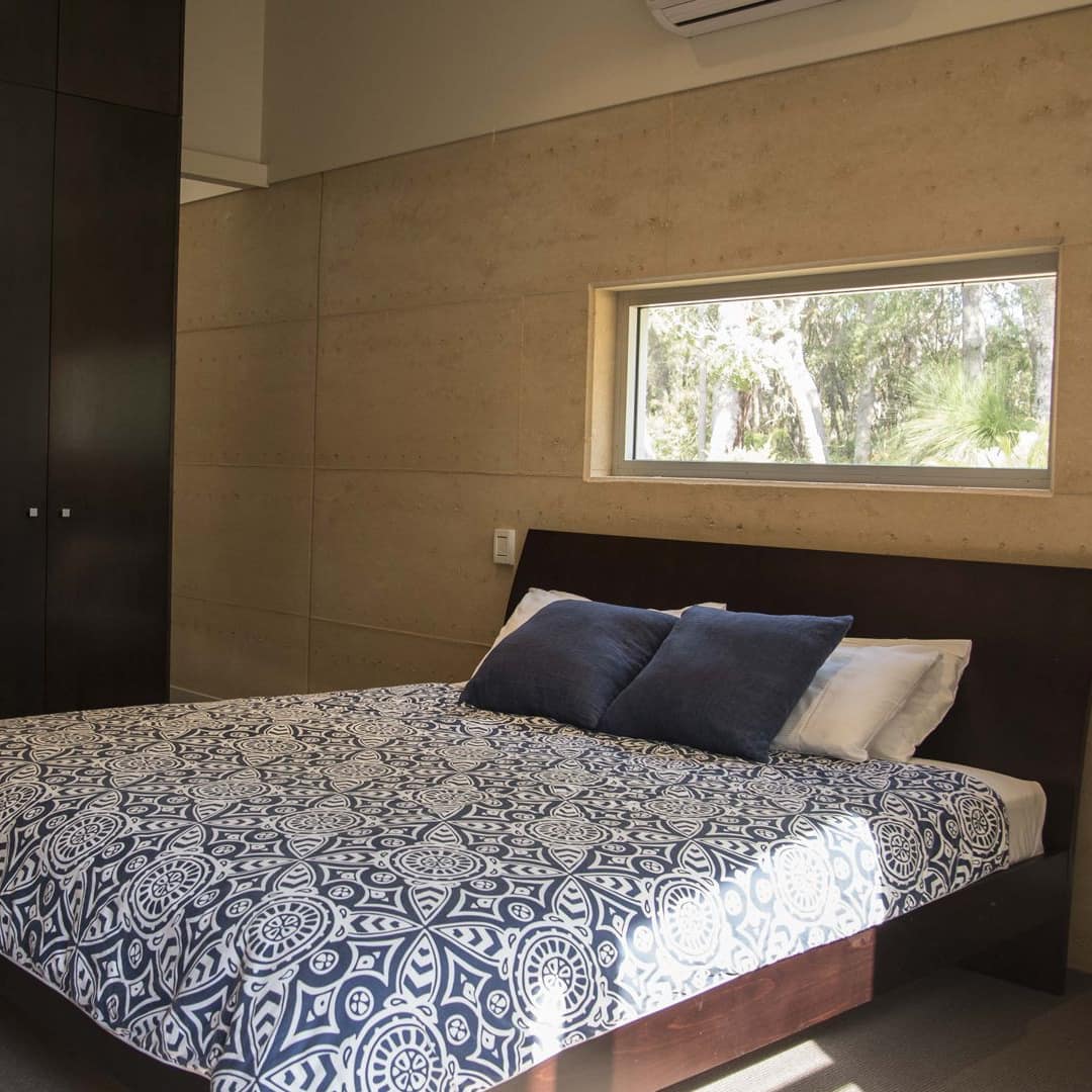 Modern bedroom with a king size bed, blue and white bedding, tall black dresser, and a wide window.
