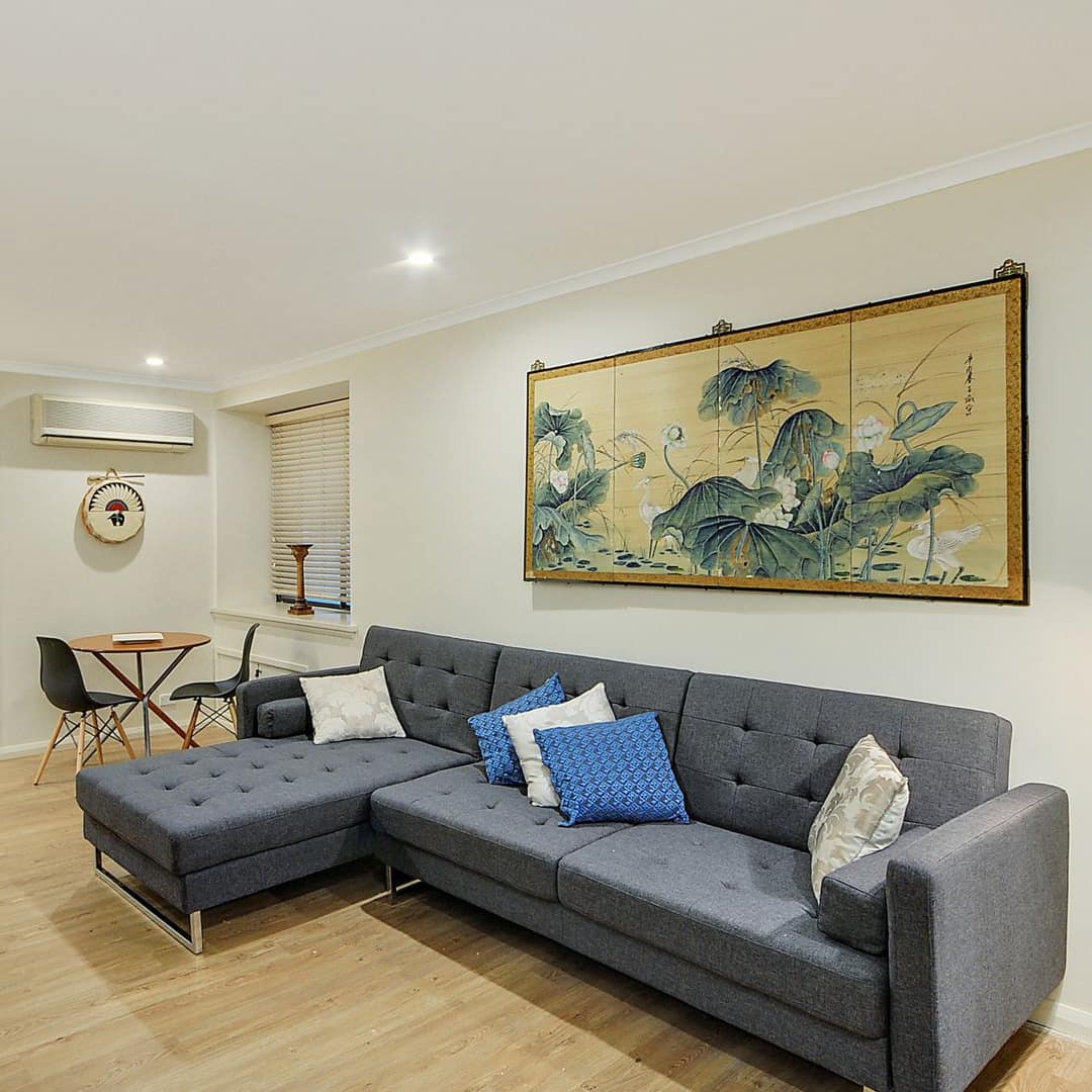 Open living room with hardwood floors, white walls, a grey sectional, wooden dining set, and Asian-inspired wood prints.