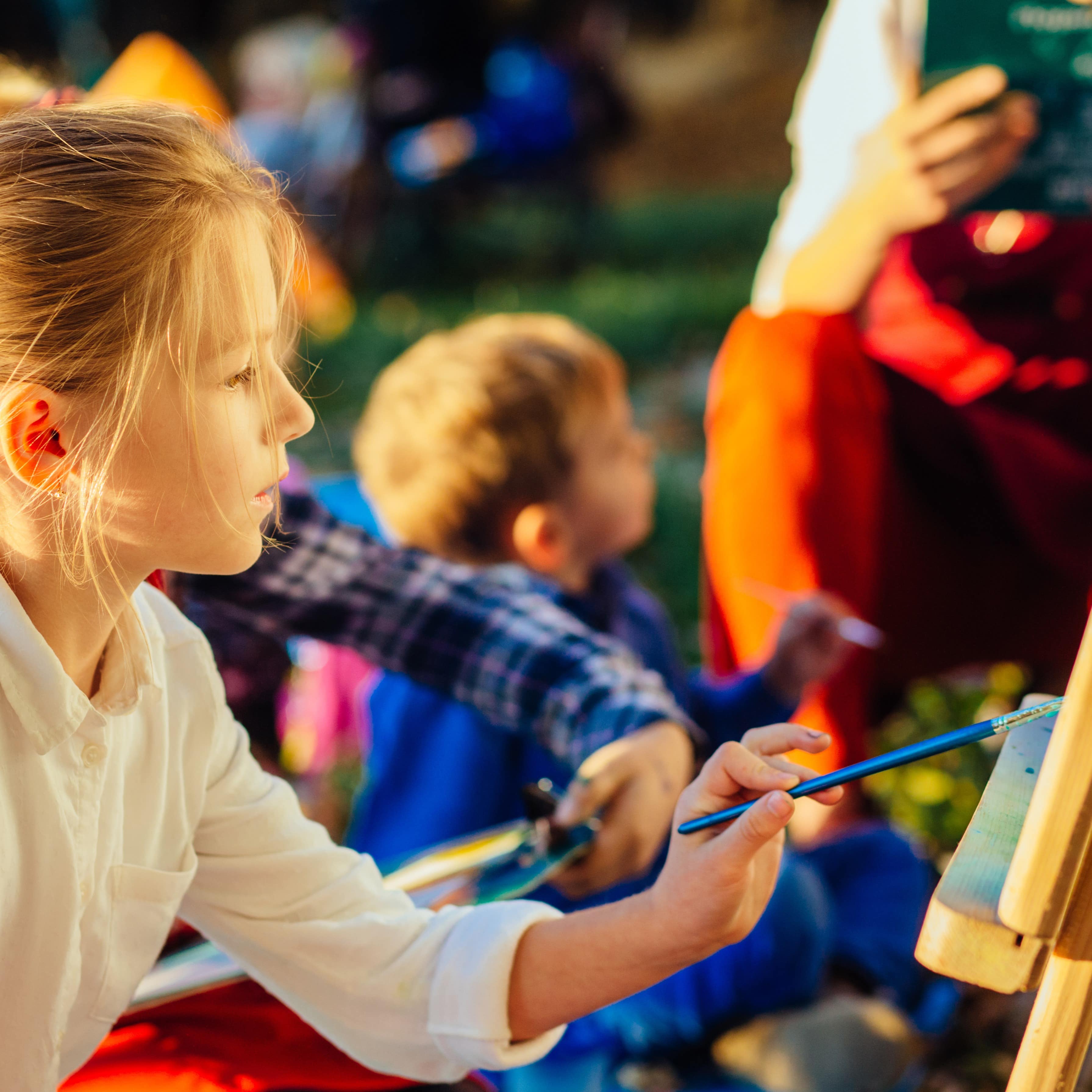Young girl at outdoor art class painting on easel