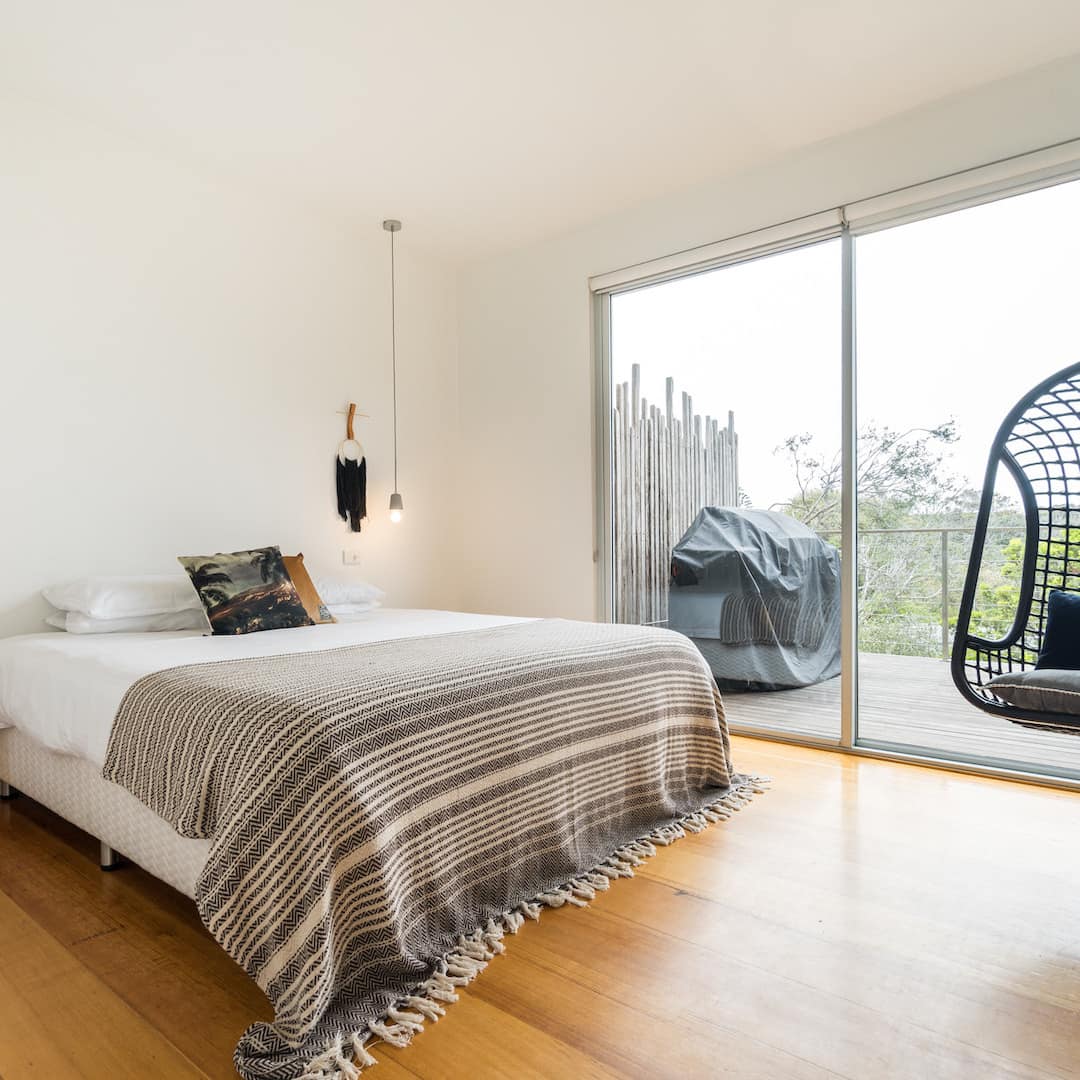 Bedroom with hardwood floors, white walls, a king size bed, white and grey bedding, and black hanging chair.