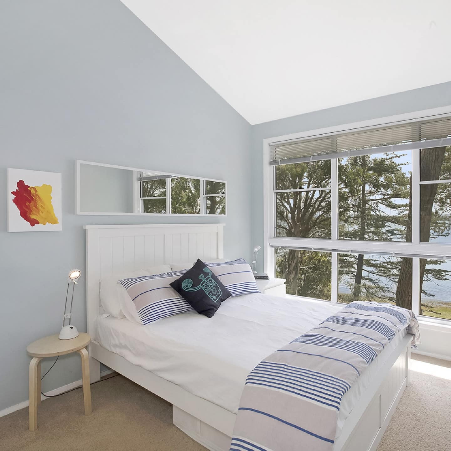 Bedroom with light blue walls, beige carpet, wide windows with ocean views, queen size bed, and blue and white bedding.