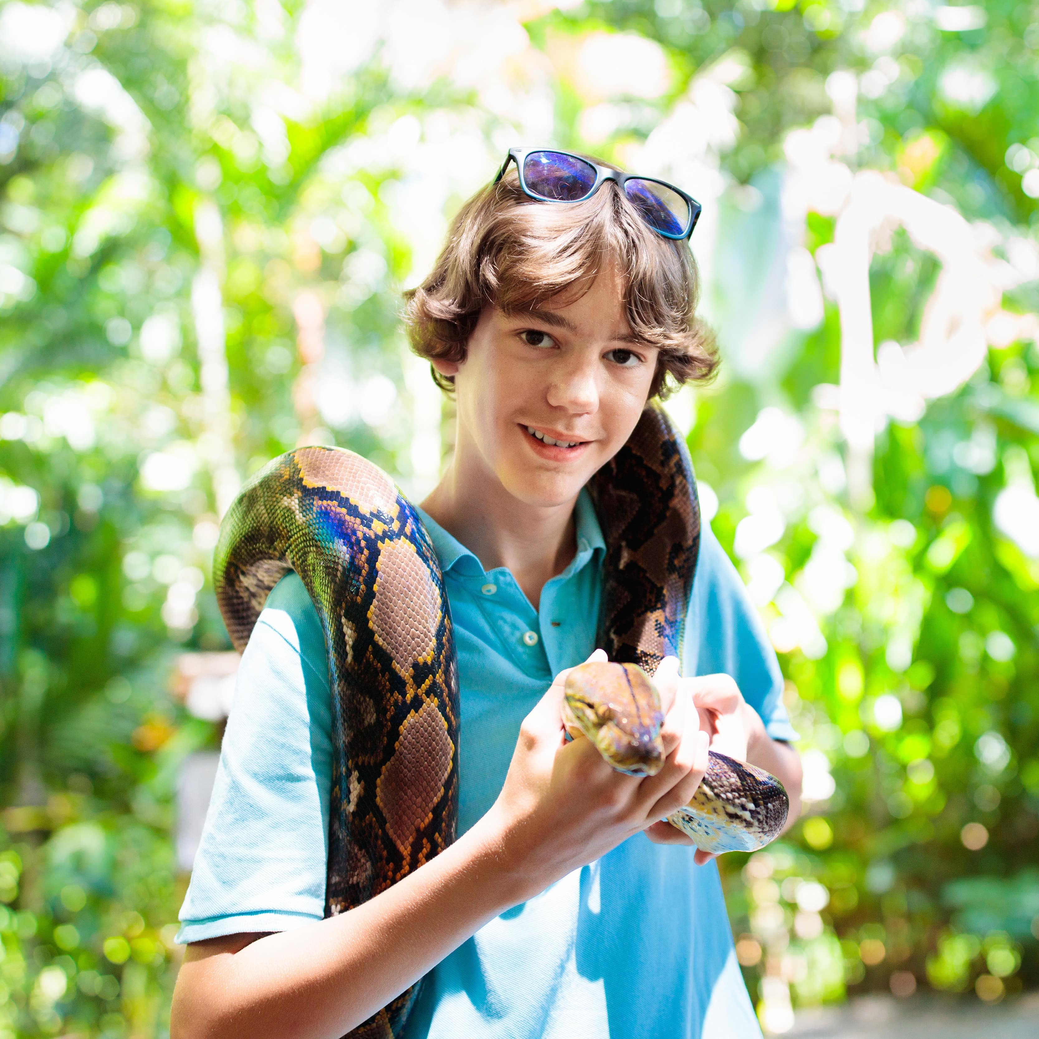 Teen boy hold python snake with green trees in background