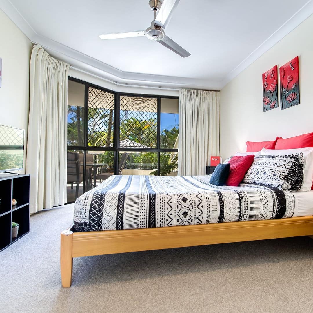 Spacious bedroom, carpeted floors, wood-framed king size bed, black, white and red bedding, flatscreen TV.