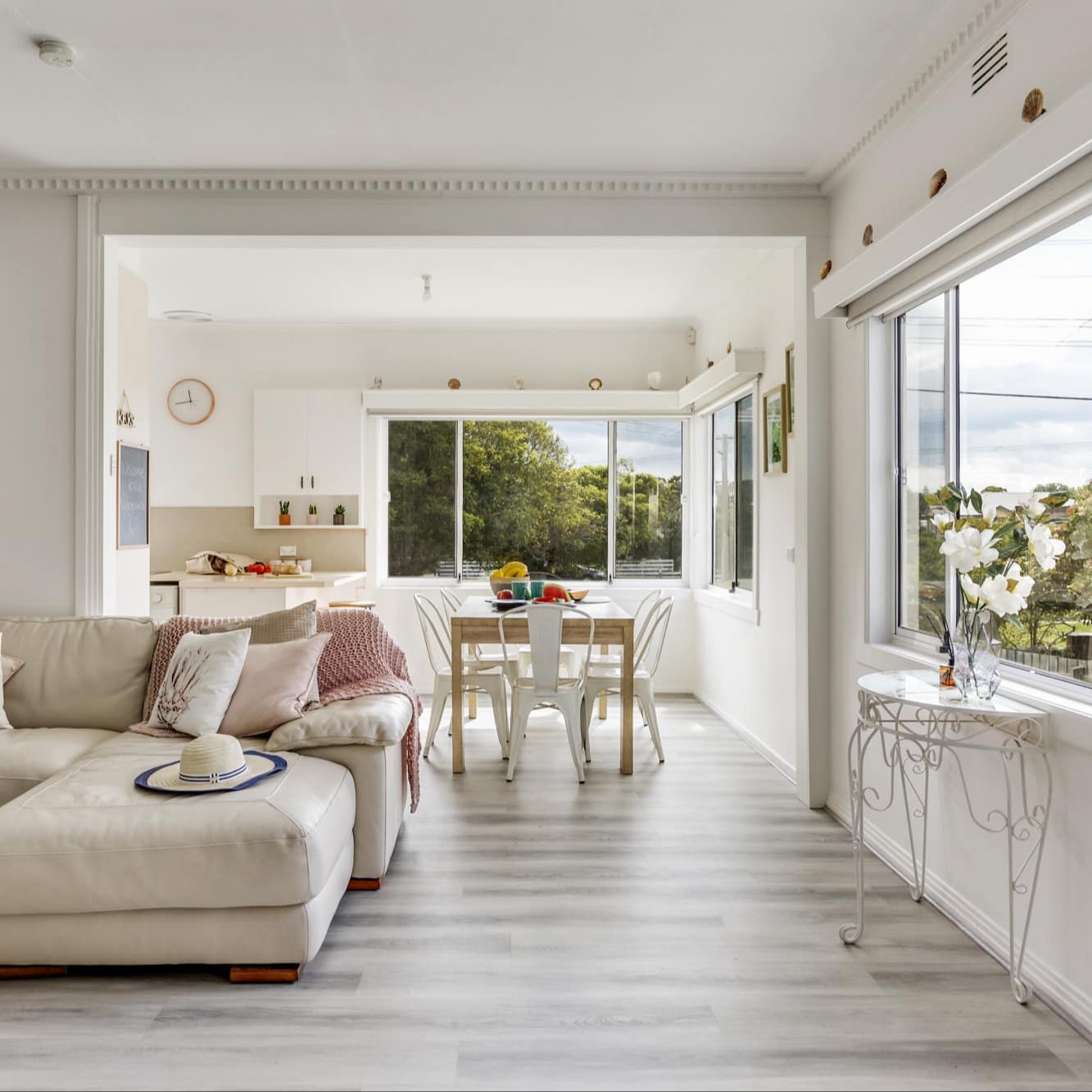 Bright and airy open, white living room with several windows, a comfy sectional and wood-look flooring