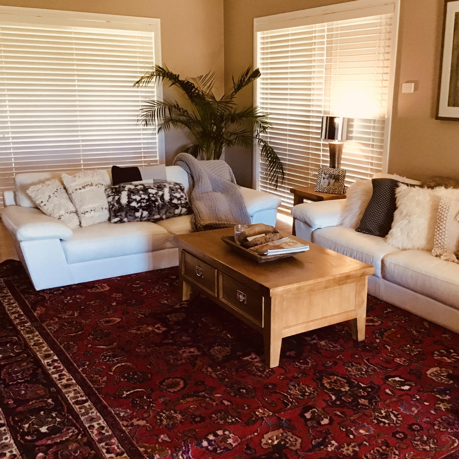 Warm living room with two white couches, plush decorative pillows, red persian rug, light wood coffee table.