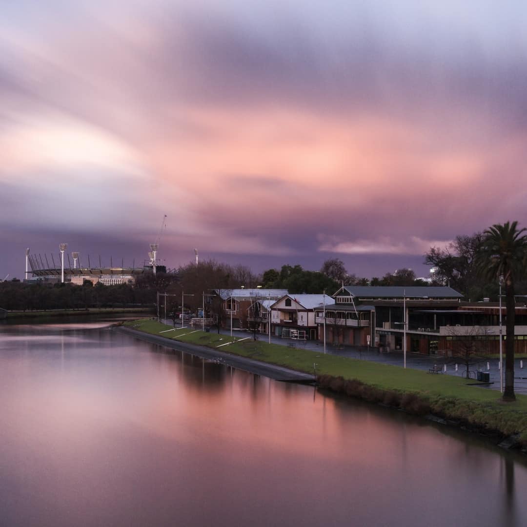 Sunset over river canal with pink and purple reflections on the water, palm trees and riverfront buildings