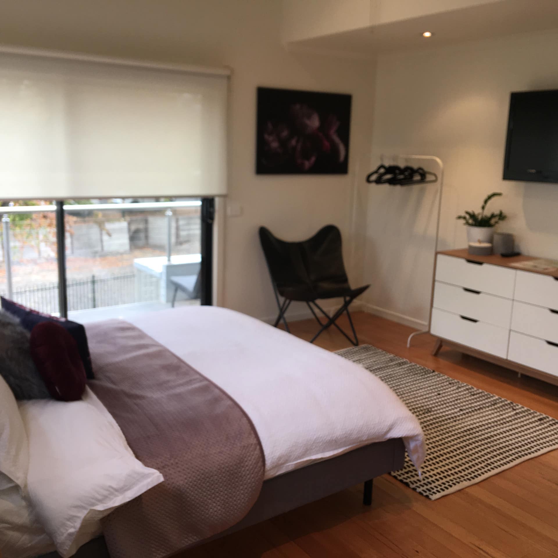 Modern, simple bedroom with a balcony view, bed, dresser, chair and flat-screen tv on the wall