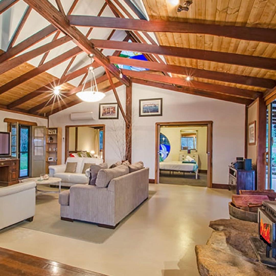 Spacious, open living room with vaulted ceilings and exposed wood beams, beige sofas, flatscreen TV, wood-burning stove.