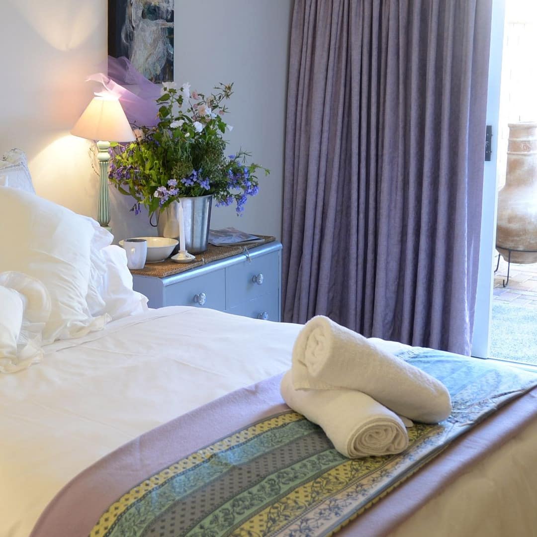 Bedroom with a queen-sized bed with white linens, plush pillows, taupe curtains and glass door to the patio with chiminea.