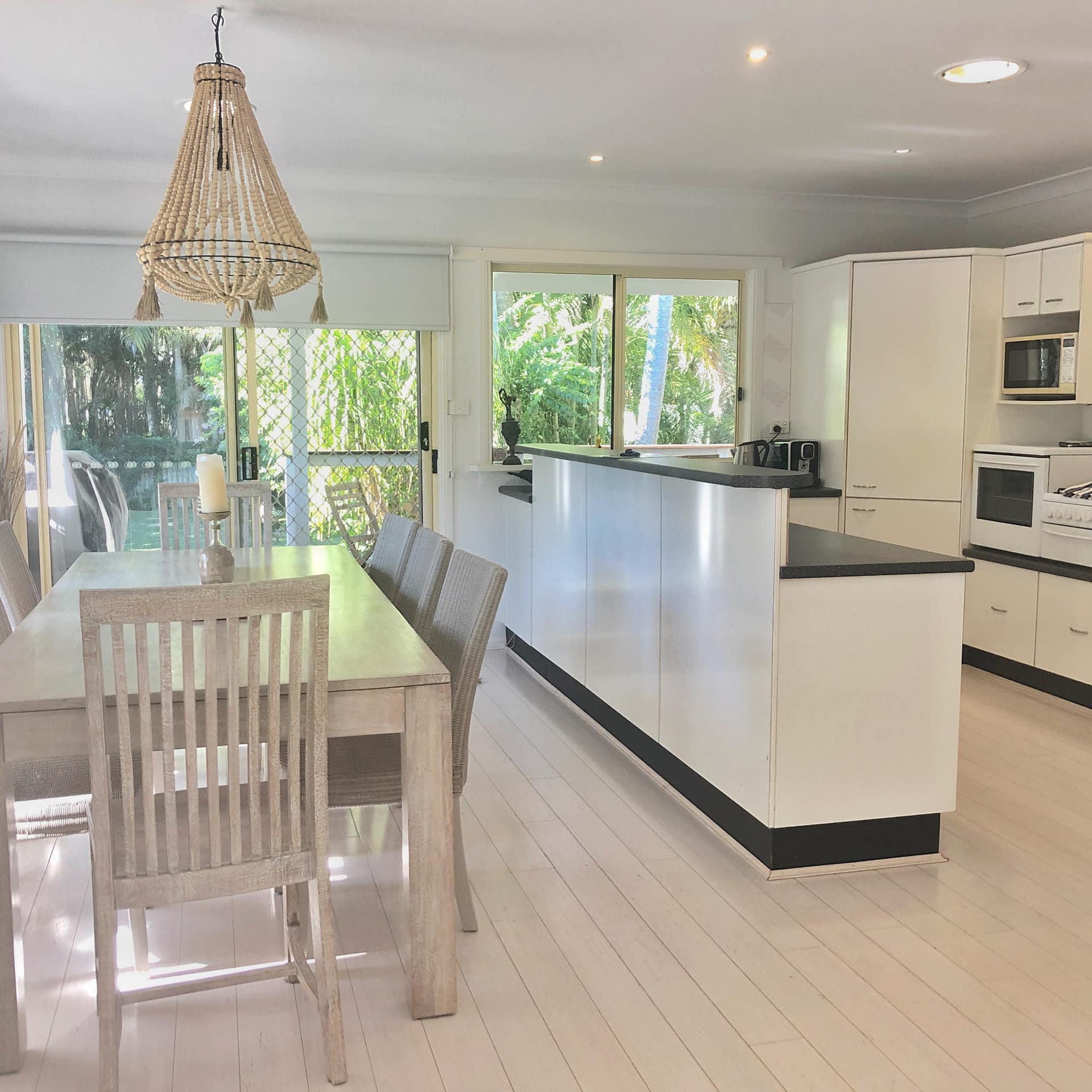 Bright kitchen with a white dining set, white cabinets, black countertops, and woven hanging light.