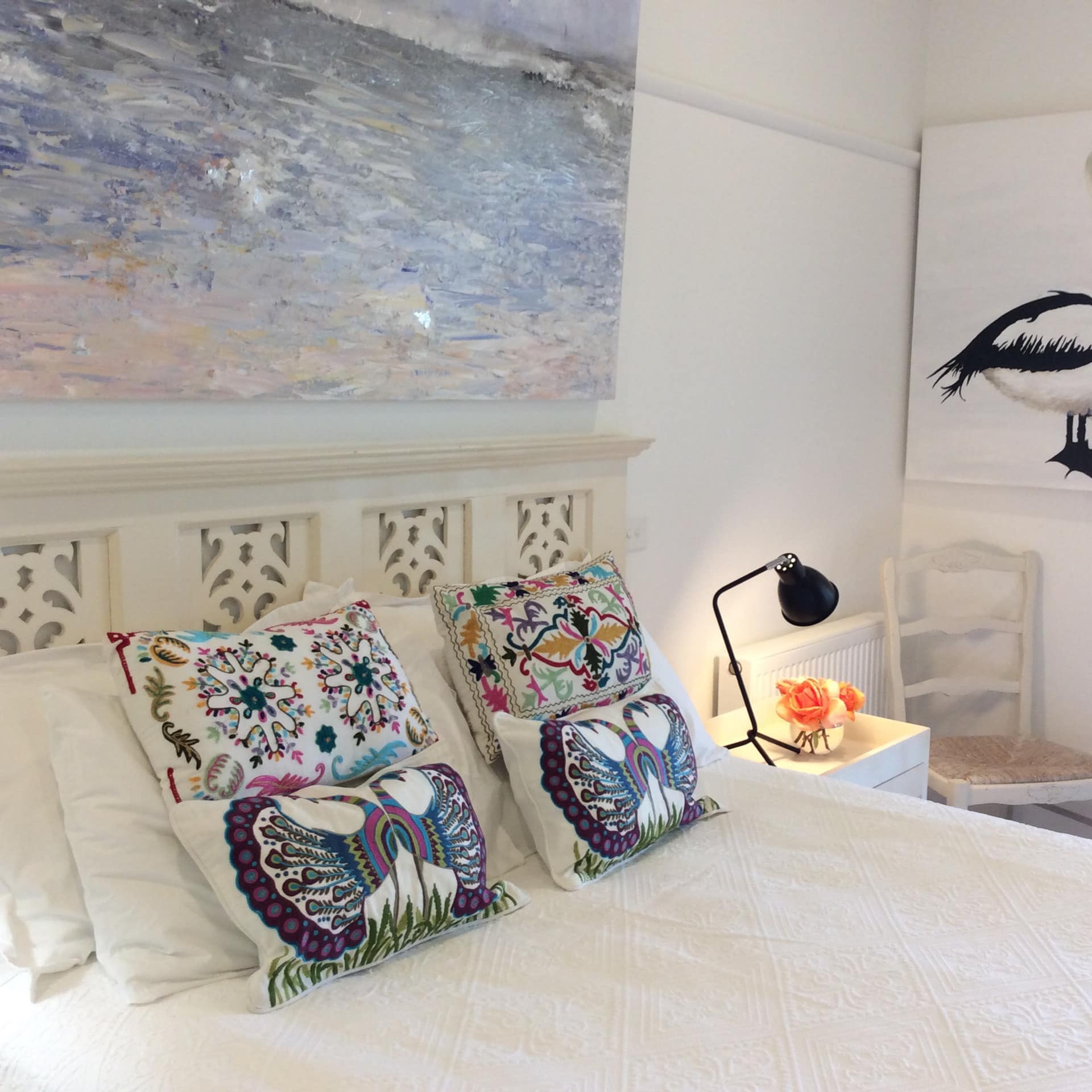 Bright bedroom with a king size bed, white bedding, colorful pillows, wicker chair, nautical art.