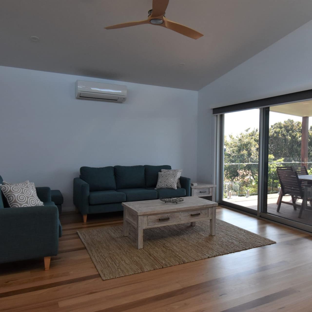Living room with hardwood floors, teal cloth sofas, distressed furniture and sliding glass windows to a covered porch.