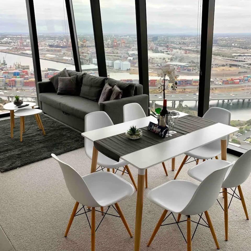 An open living and dining room with floor to ceiling panoramic windows with views of Melbourne's skyline.