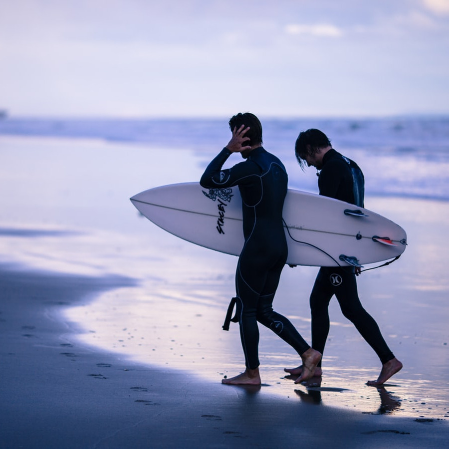 A blue-tone monochromatic view of two early morning surfers walking along a calm shoreline of Torquay Beach. 