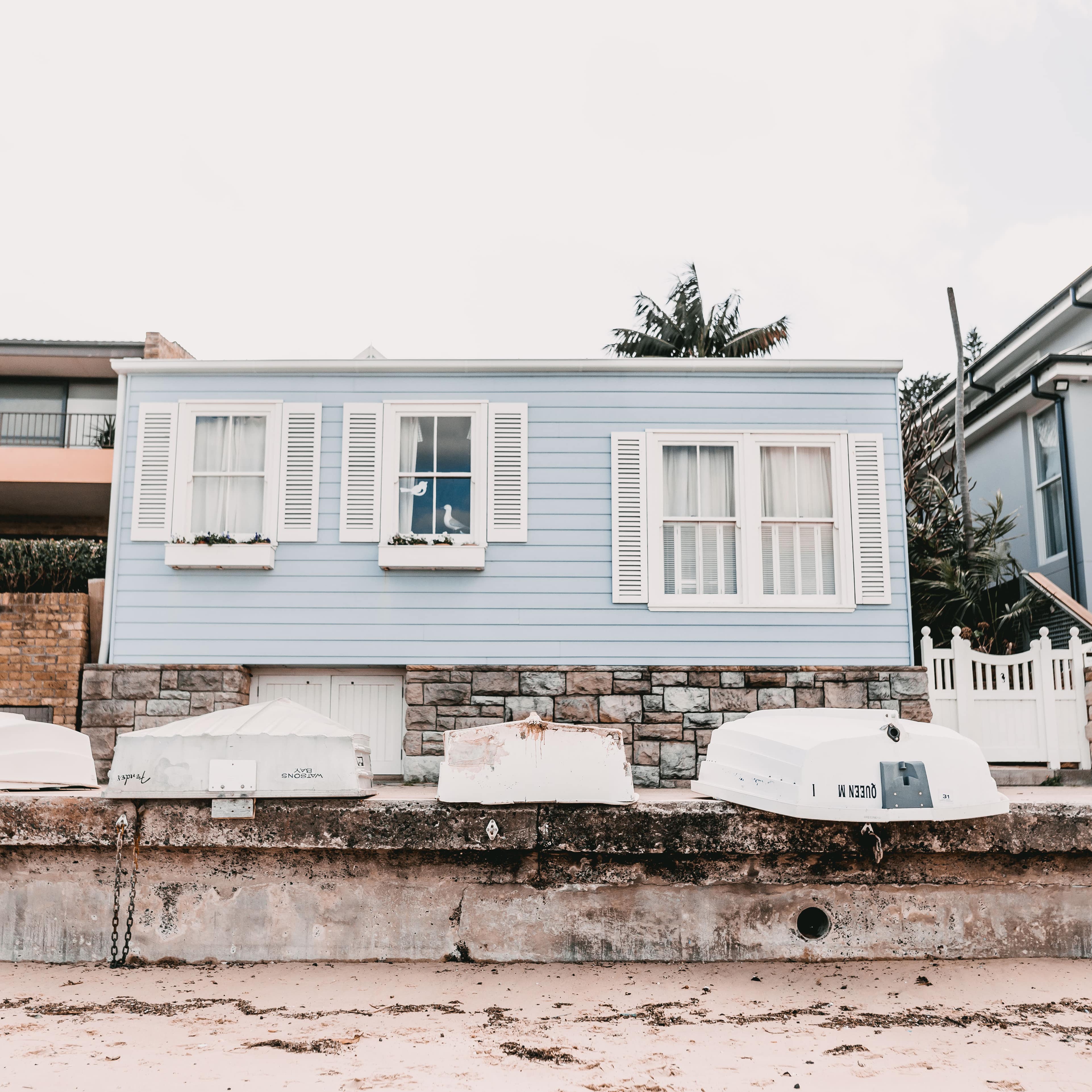 Beachfront cottage in Sydney with blue siding, white shutters, flower boxes and a stone foundation with small boats