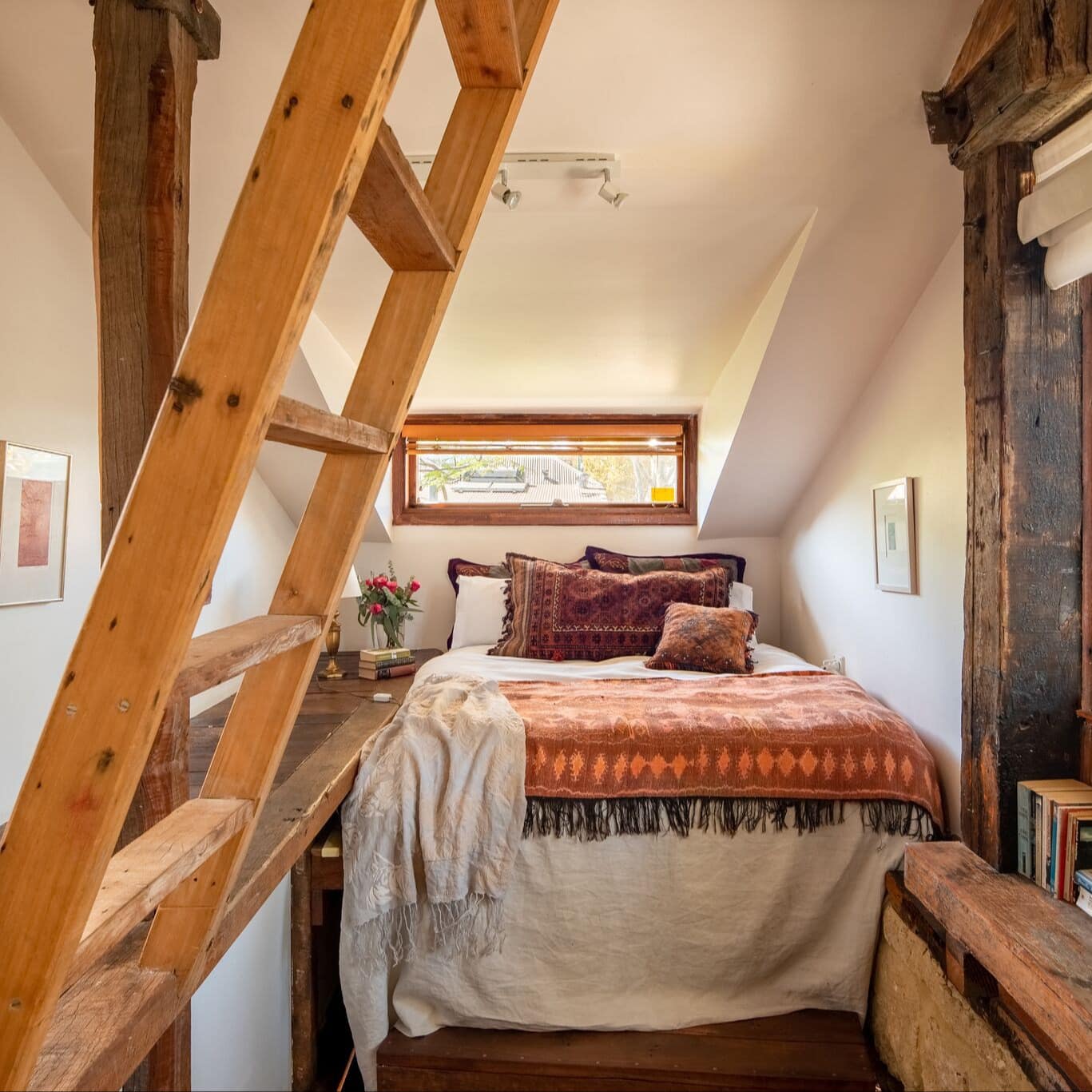 Rustic bedroom with hardwood floors, white walls, twin bed, white and orange bedding, natural wood accents, wide windows.