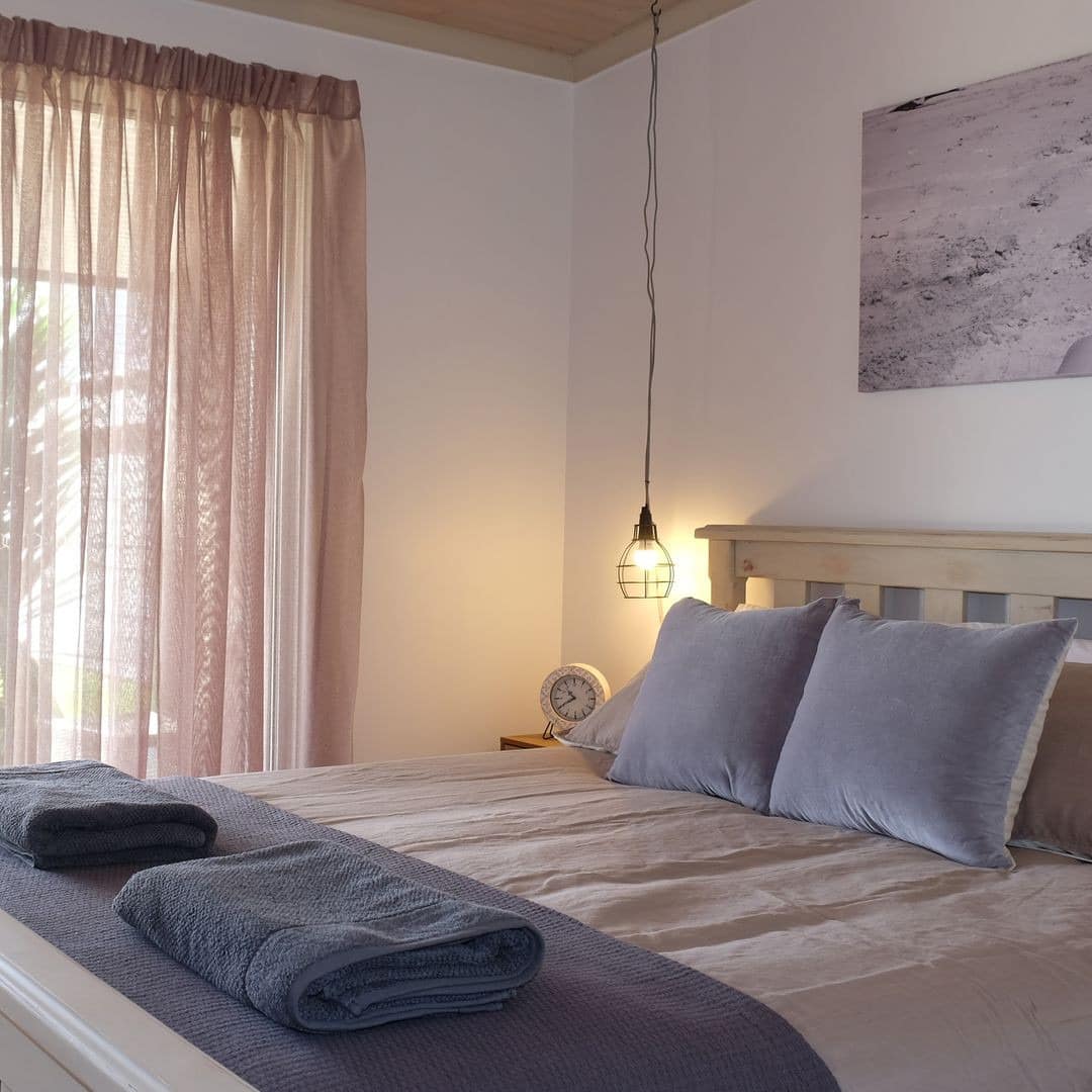 Warm bedroom with a king size bed, tan and grey bedding, sliding glass doors to patio space with pink sheer curtains.