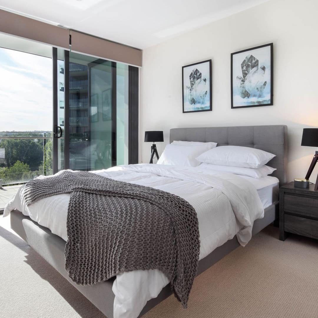 Bedroom with beige carpet, a king size bed, white and grey bedding, and sliding glass doors to attached balcony.