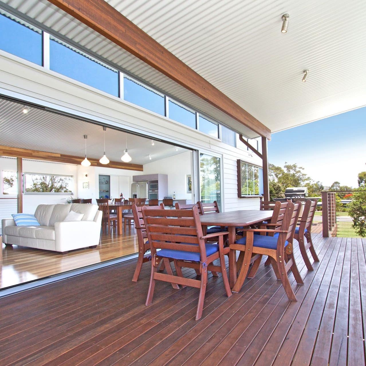 Covered veranda with wood dining set, and wide sliding glass doors open into open living and dining room of the home.